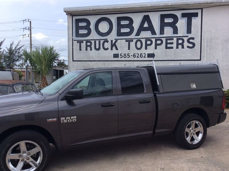 Dark pickup truck parked in front of a Bobart Truck Toppers sign.