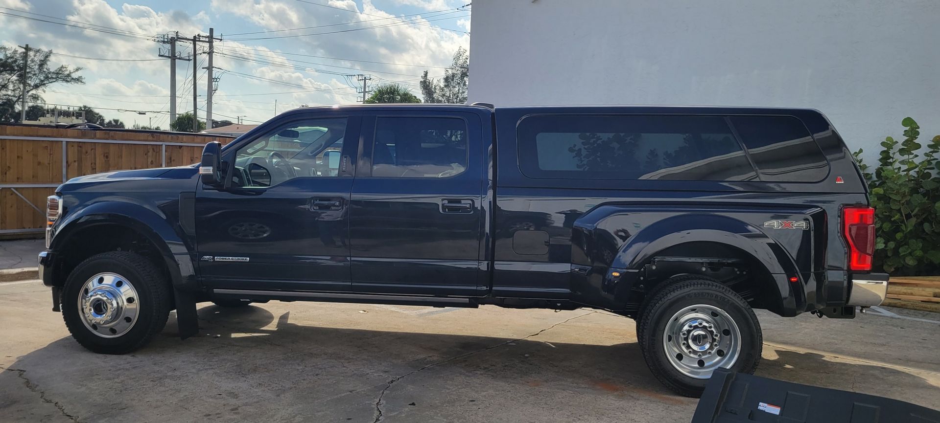Dark blue pickup truck with a camper shell parked in a lot under cloudy sky