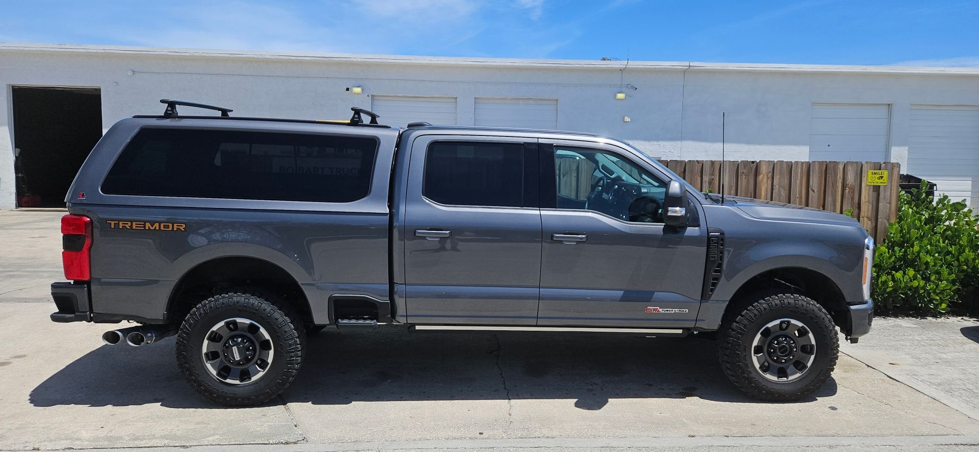 Gray pickup truck with camper shell parked on a sunny street beside a stucco wall