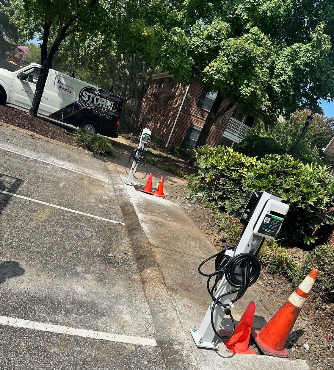 Outdoor parking area with a parked car, electric vehicle charger, and orange traffic cones near a sidewalk.