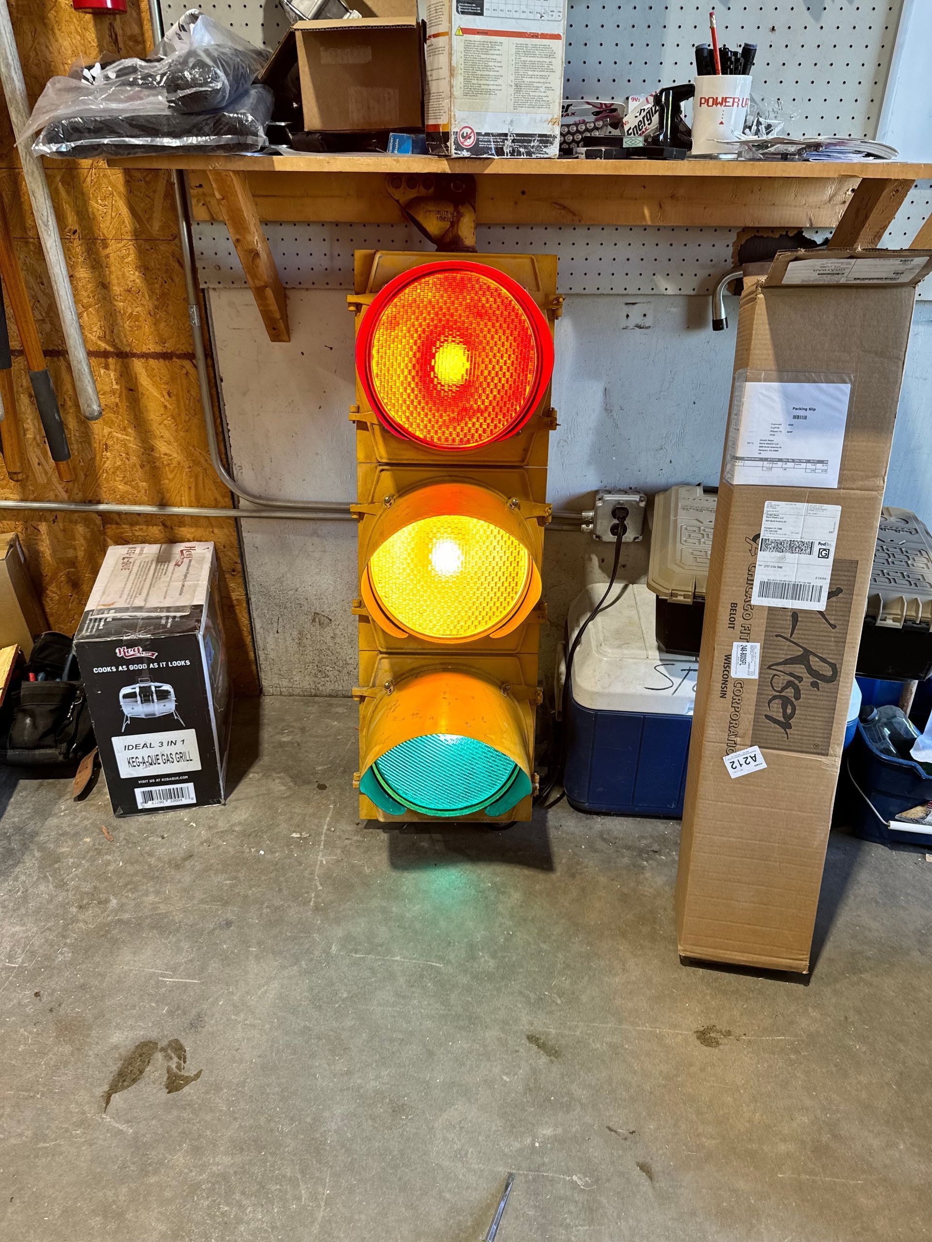 Stacked red, yellow, and green traffic lights on a workshop shelf in a cluttered garage
