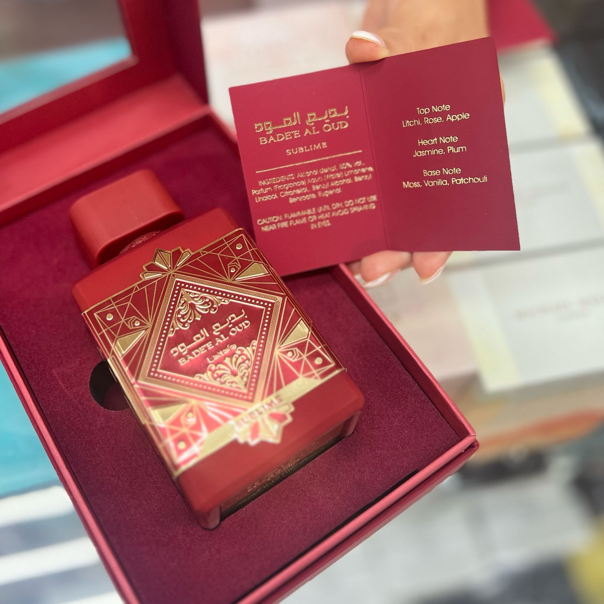 A person is holding a bottle of perfume in a red box