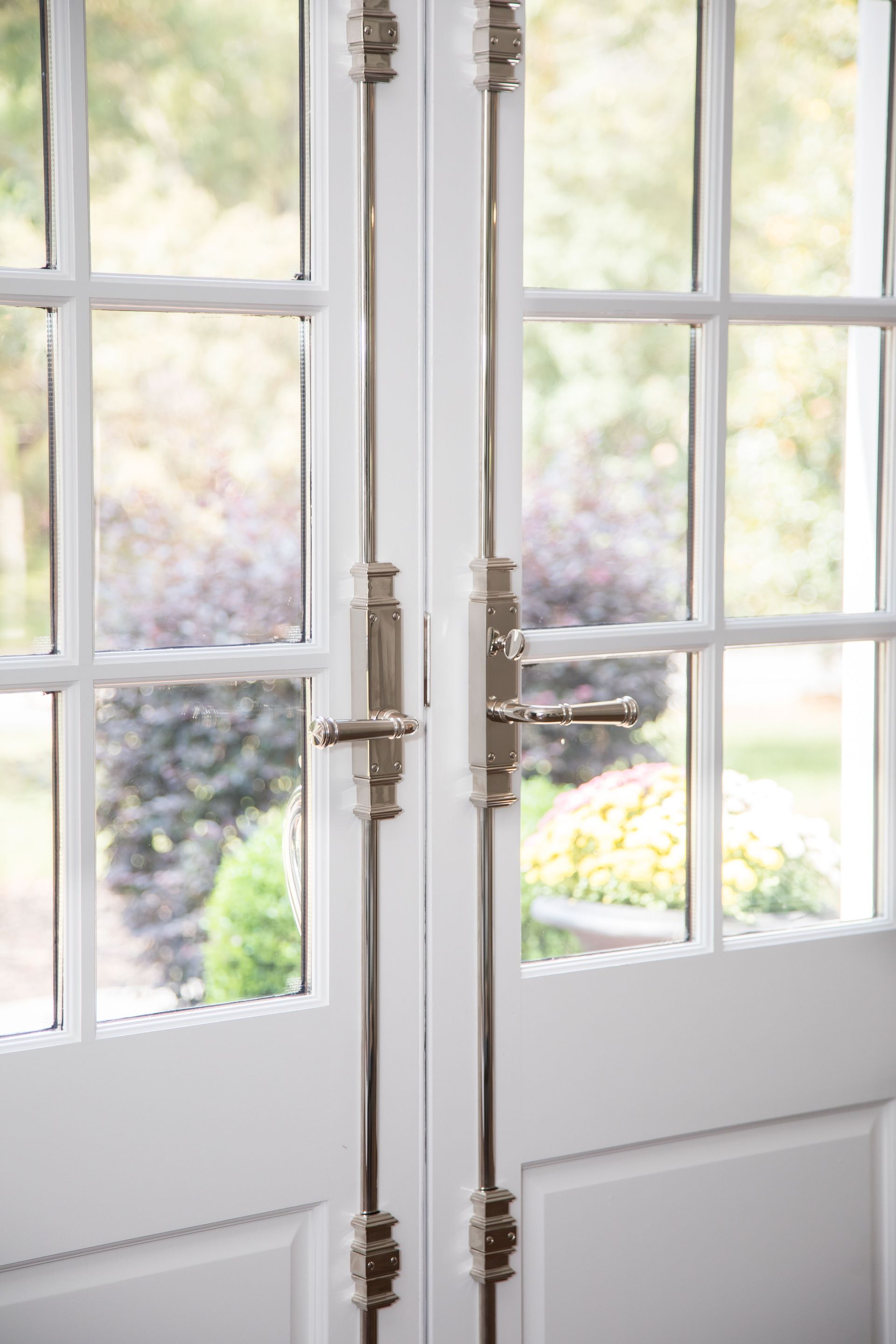 A close up of a pair of white french doors with a view of a garden.