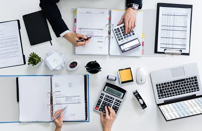 A group of people are sitting at a table using calculators and laptops.