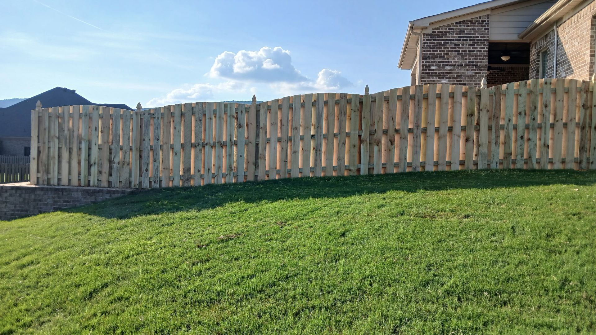 Wooden fence in front of house with a grassy lawn and cloudy sky.