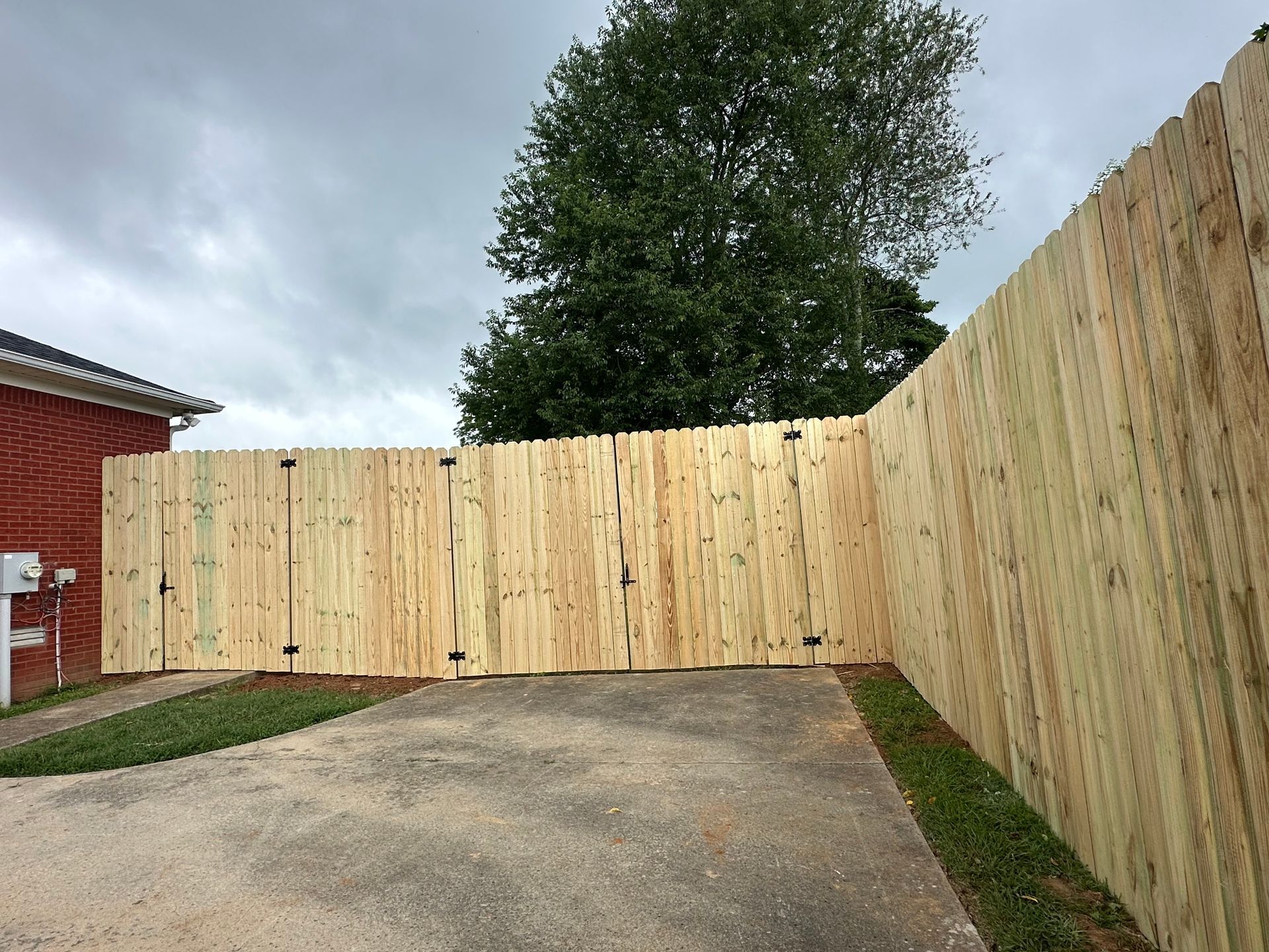 Wooden privacy fence encloses a driveway and part of a house under a cloudy sky.