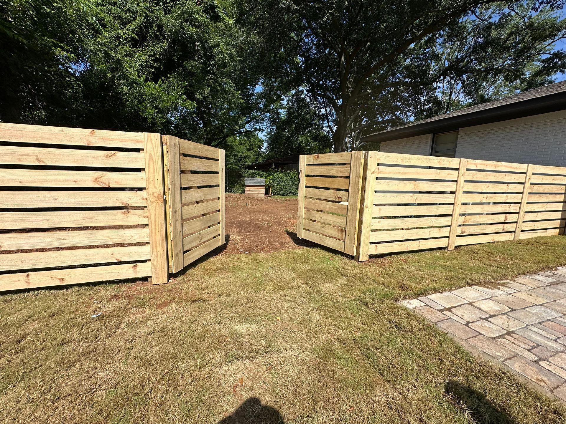 Wooden fence with open gate on a grassy lawn. Building in the background.
