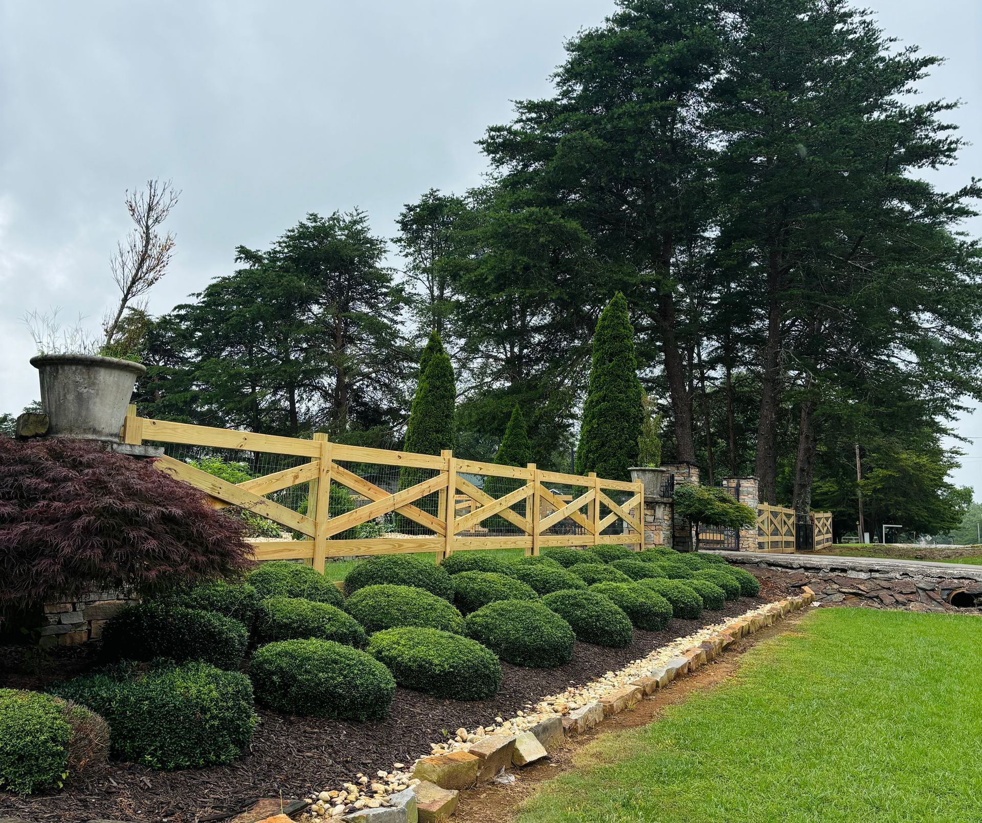 Wooden fence with landscaped garden and mature trees.
