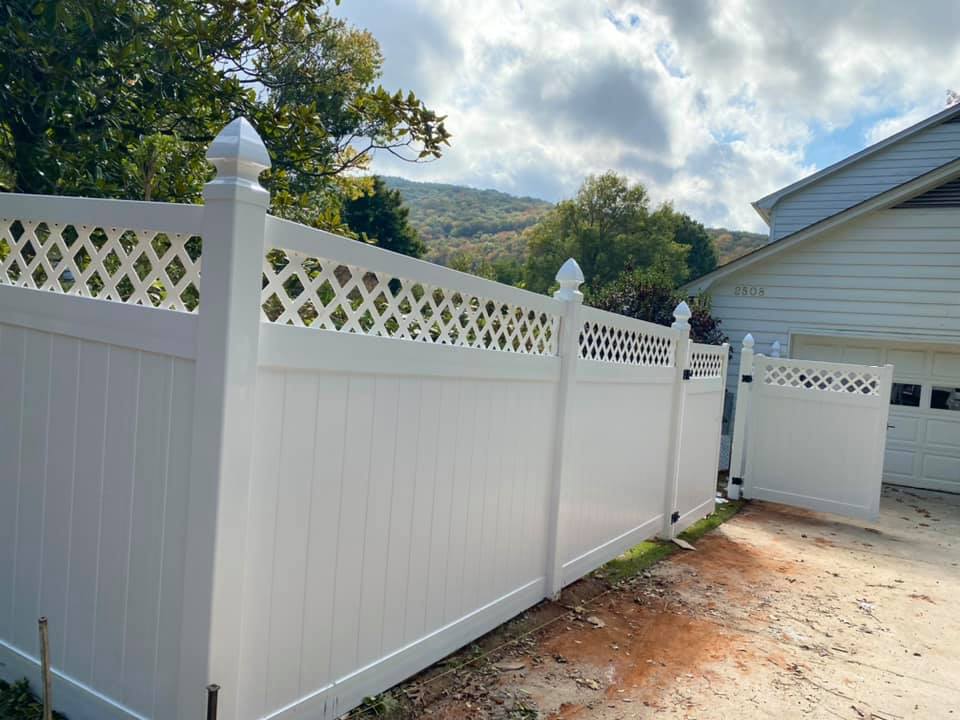 White vinyl fence with lattice top in front of a house and trees.