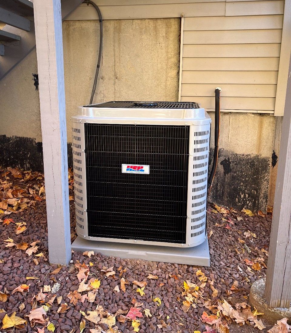 A black and white air conditioner is sitting on top of a pile of leaves.