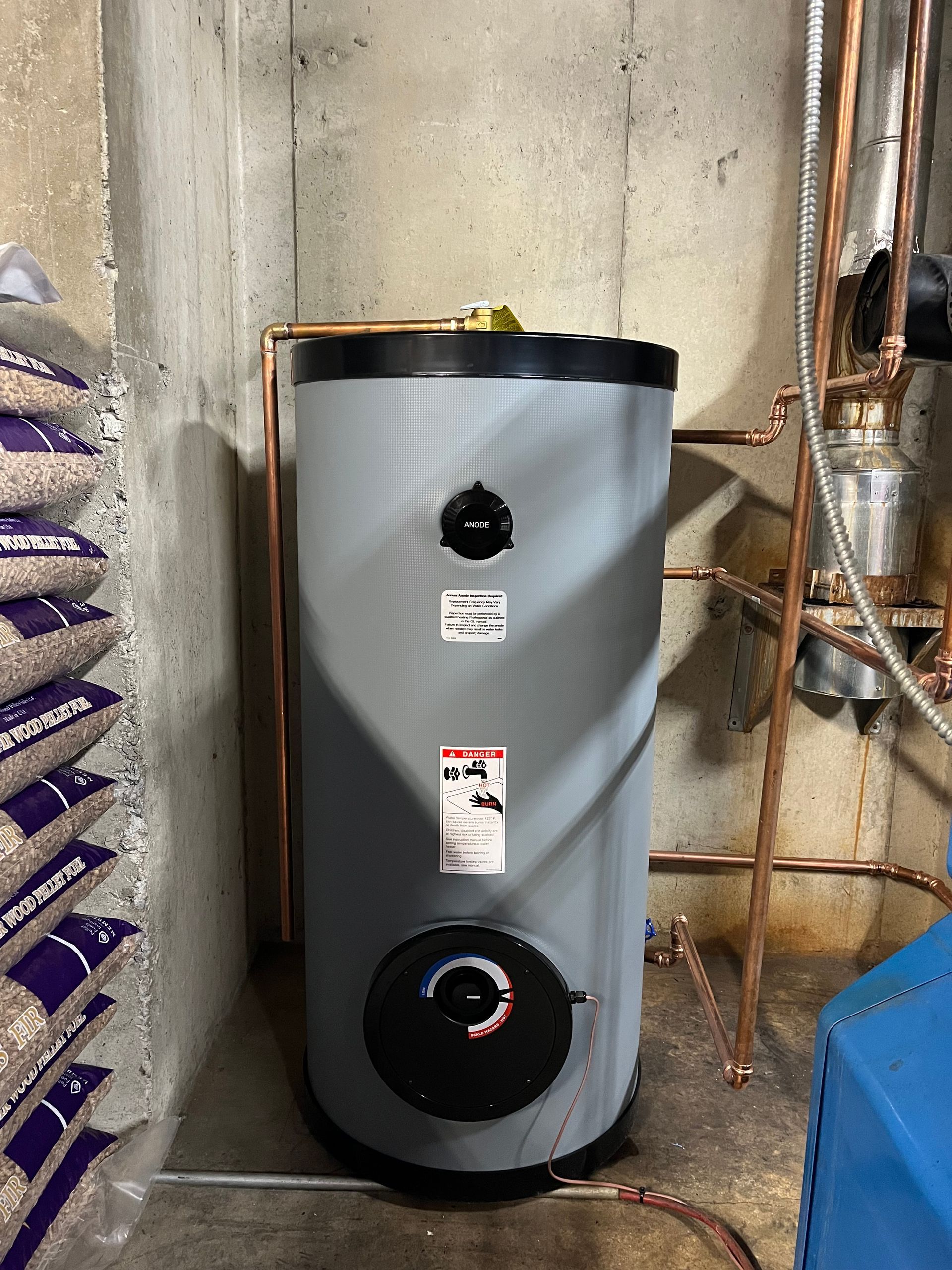 A water heater is sitting in a basement next to a pile of pellets.