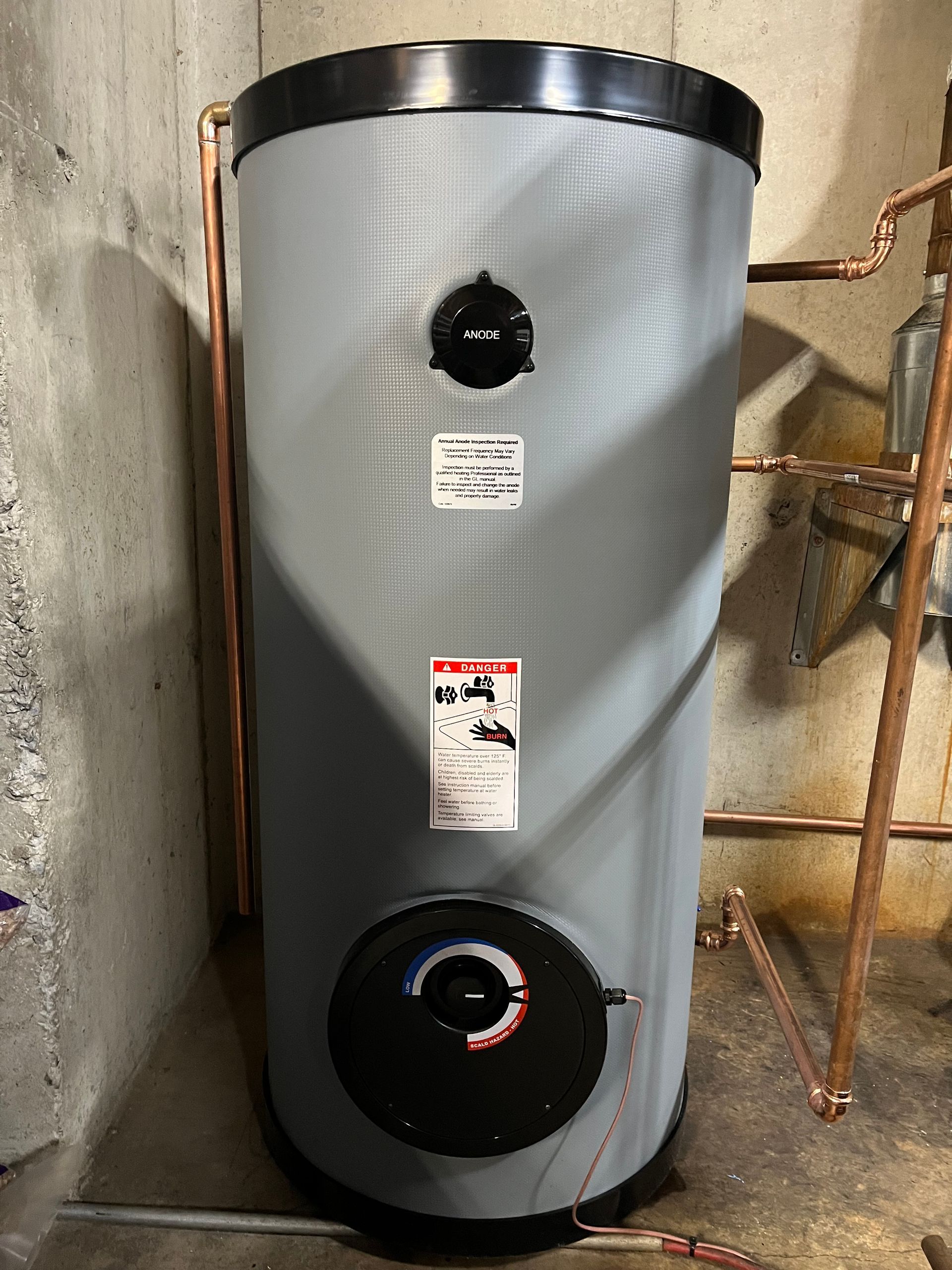 A large gray water heater is sitting in a basement next to copper pipes.