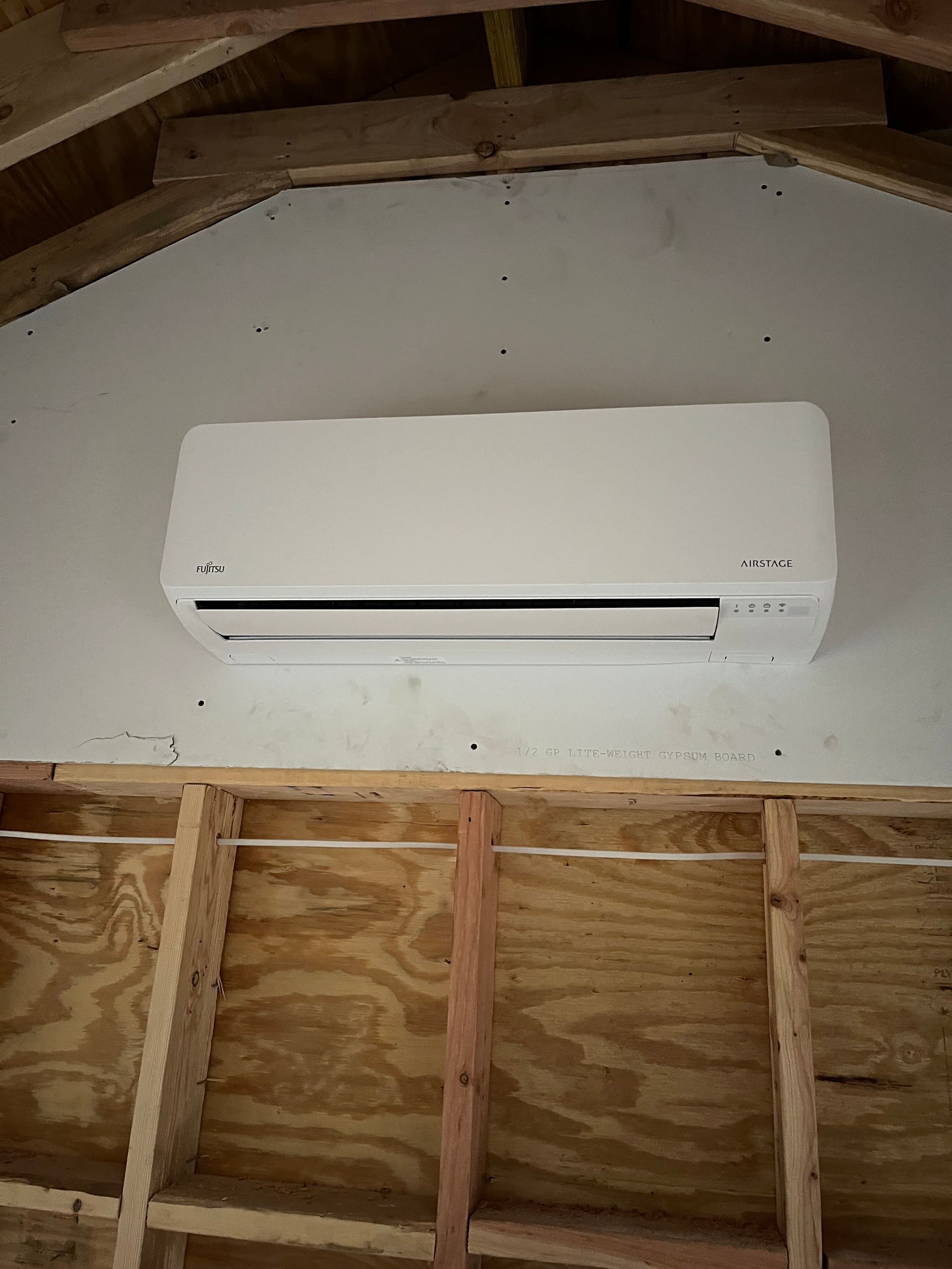 A white air conditioner is hanging from the ceiling of a building under construction.