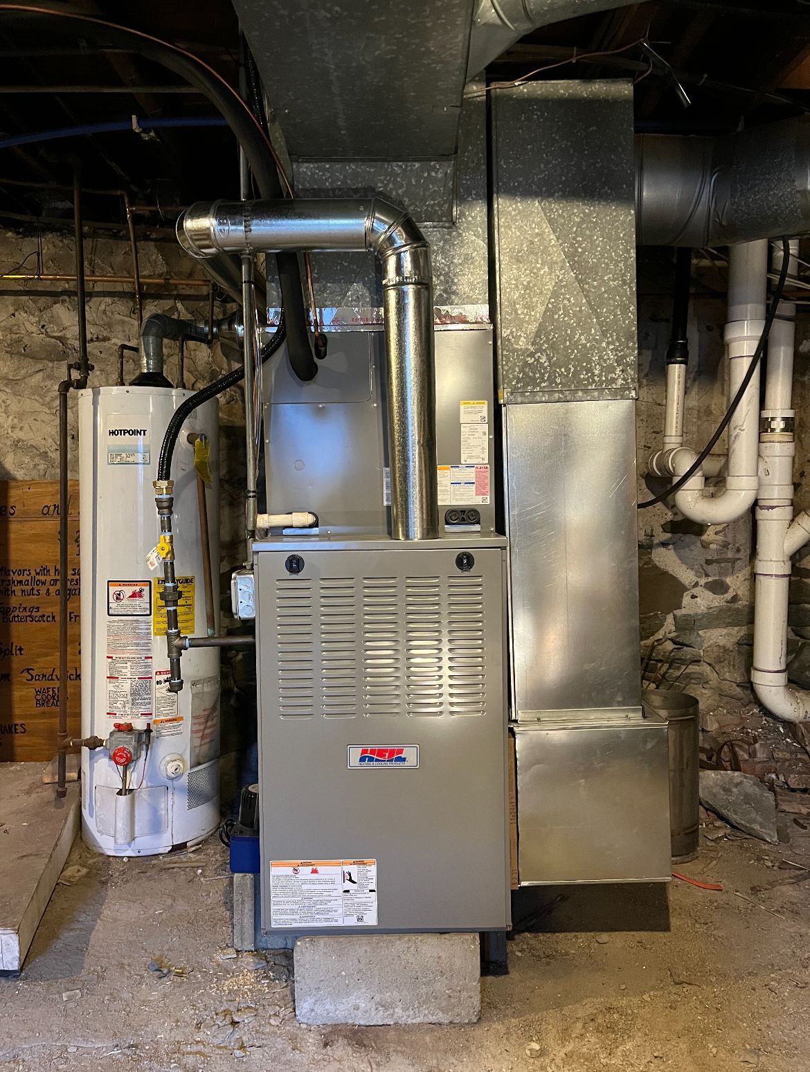 An air conditioner is sitting in a basement next to a water heater.