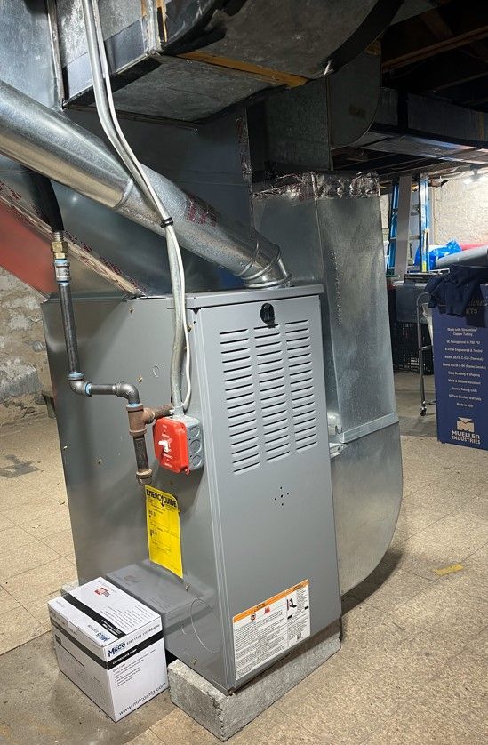 A furnace is sitting in a basement next to a box of batteries.