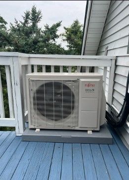 A white air conditioner is sitting on a blue deck next to a house.
