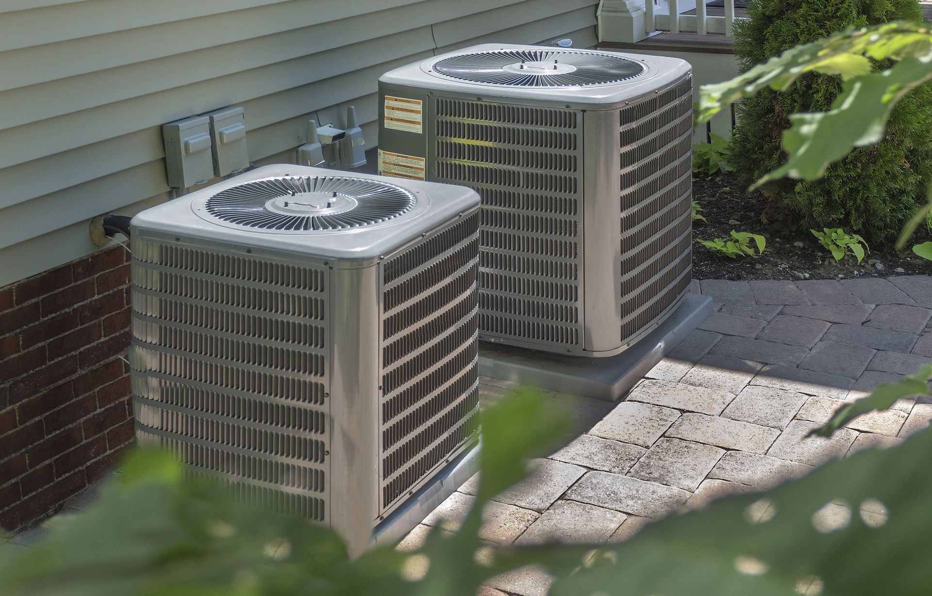 Two air conditioners are sitting on the side of a house.