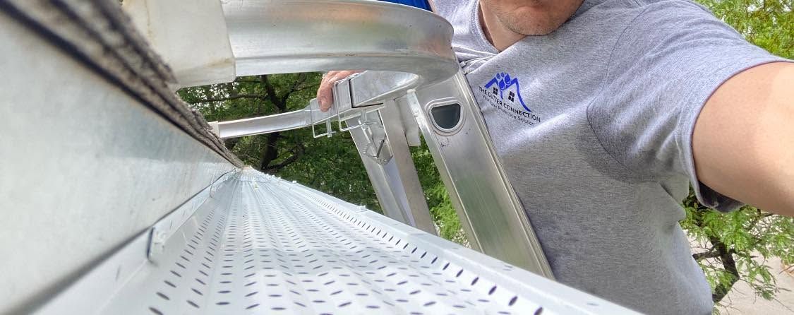 Person repairing a white gutter on a house exterior while standing on a ladder