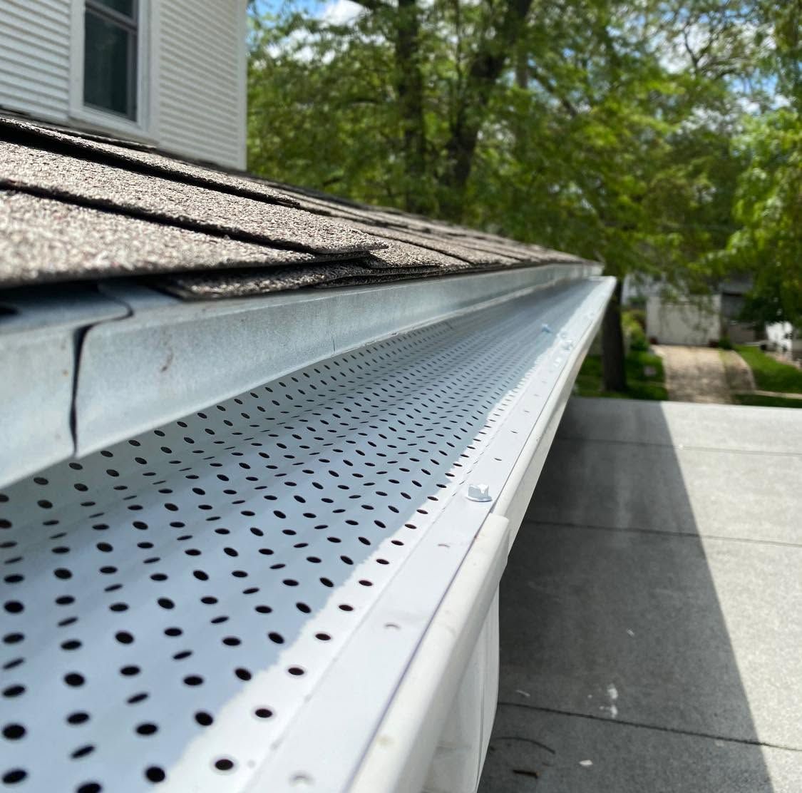 Gutter and roof edge with perforated leaf guard beside a driveway and trees