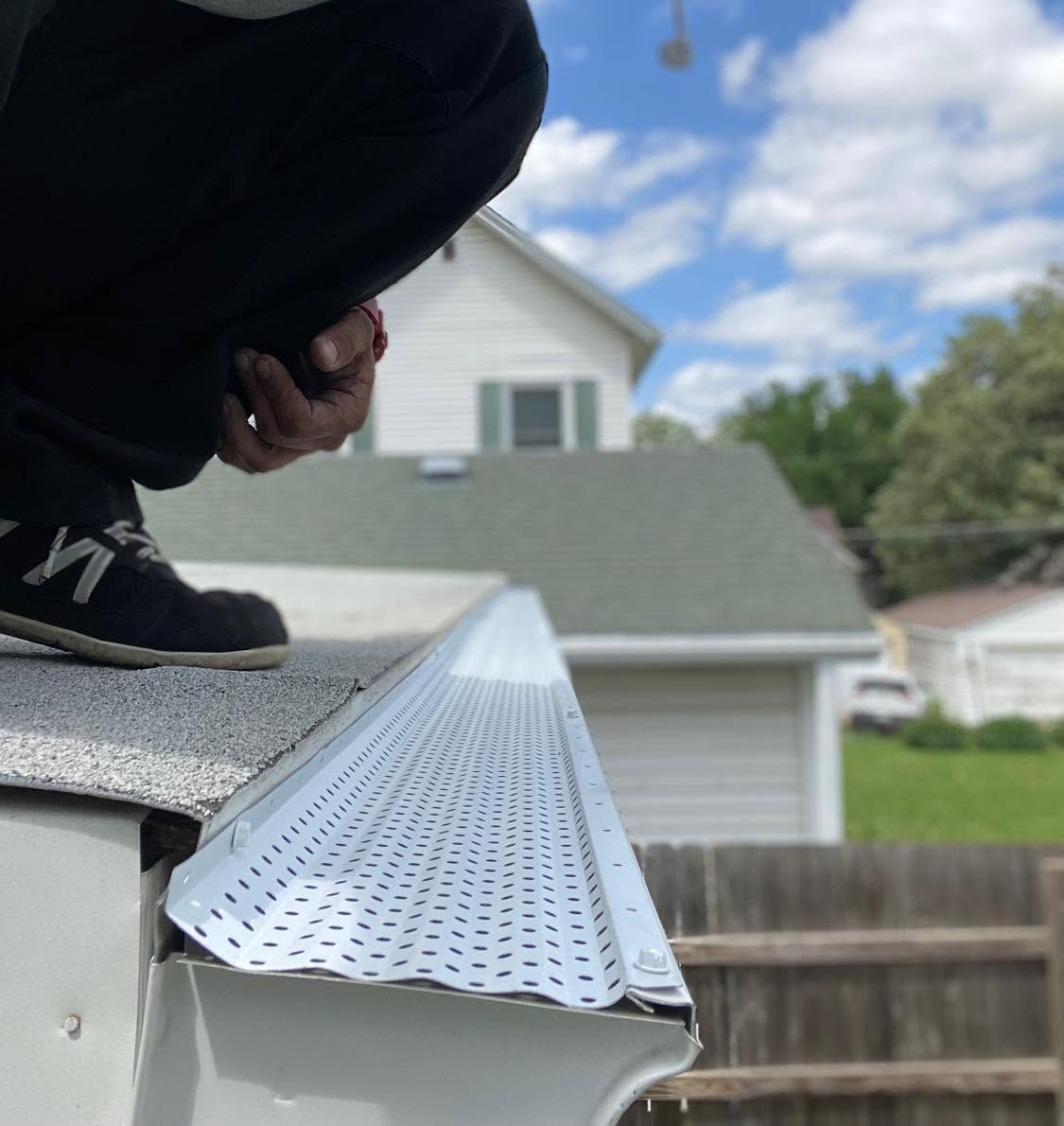 Worker installing white gutter guard on a house roof edge