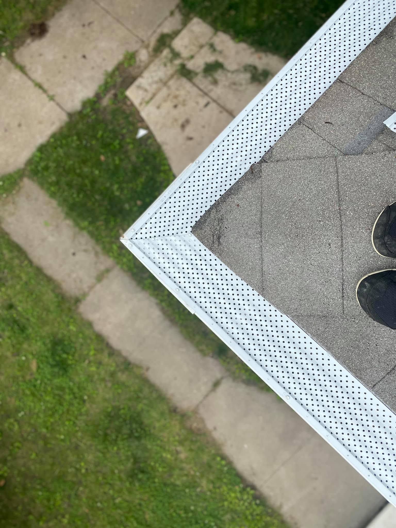 Corner of a gray rooftop with white perforated trim beside a grassy path and paving stones.