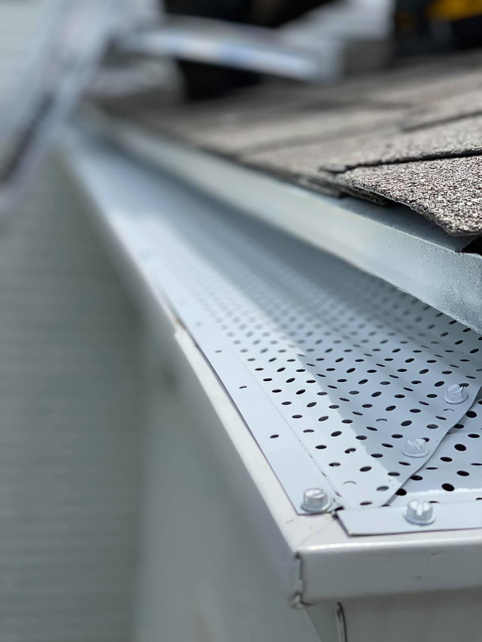 Close-up of a metal roof gutter with perforated guard under gray shingles