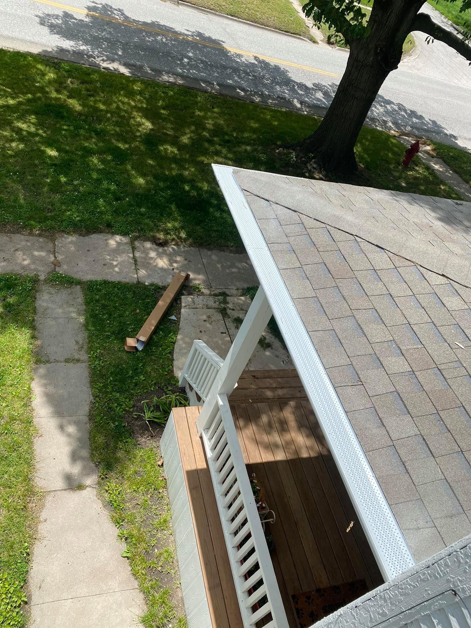 Porch roof and railing beside a grassy yard, sidewalk, and tree.