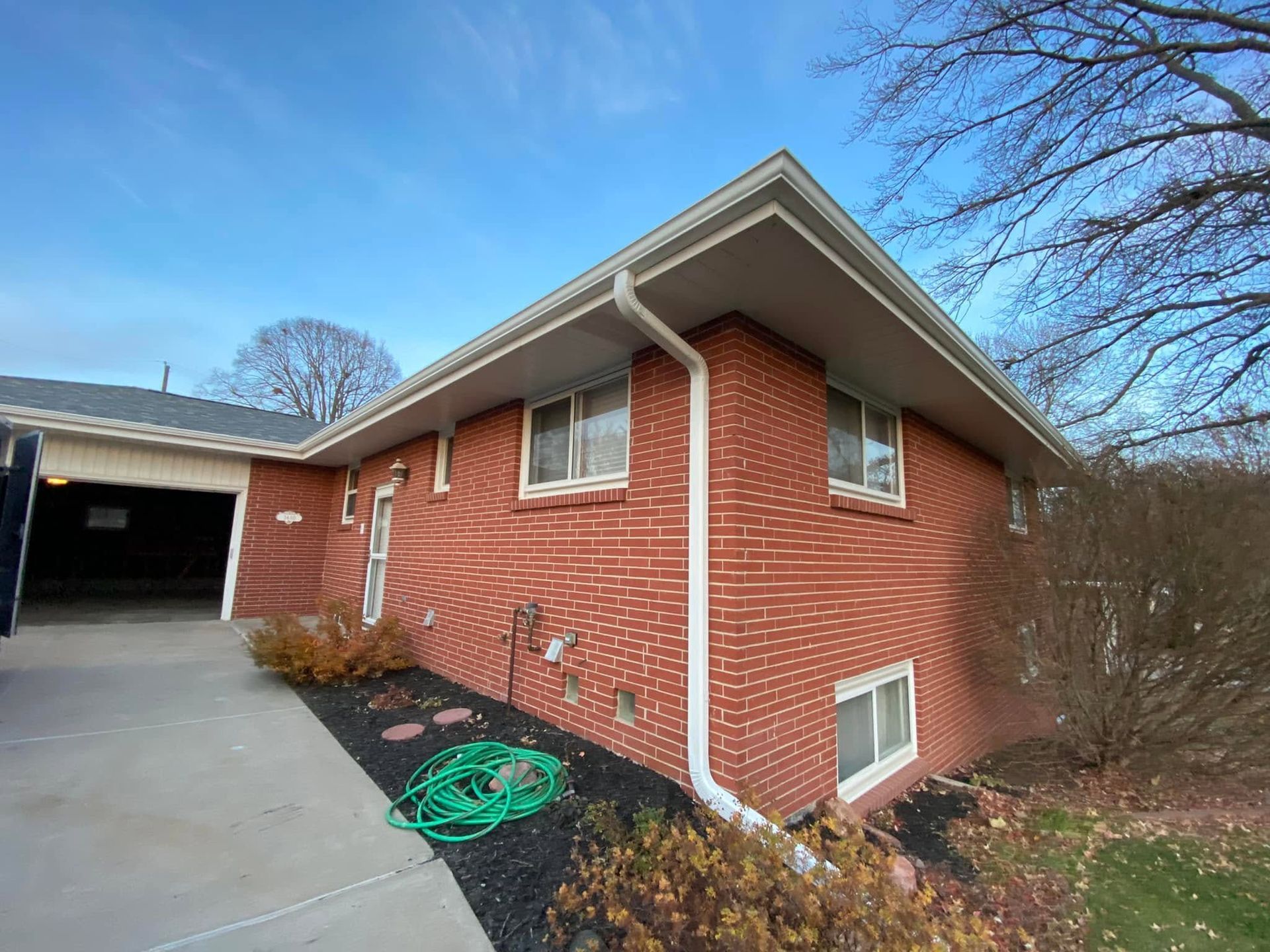 Brick house exterior with white trim, side driveway, and a garage under a blue sky