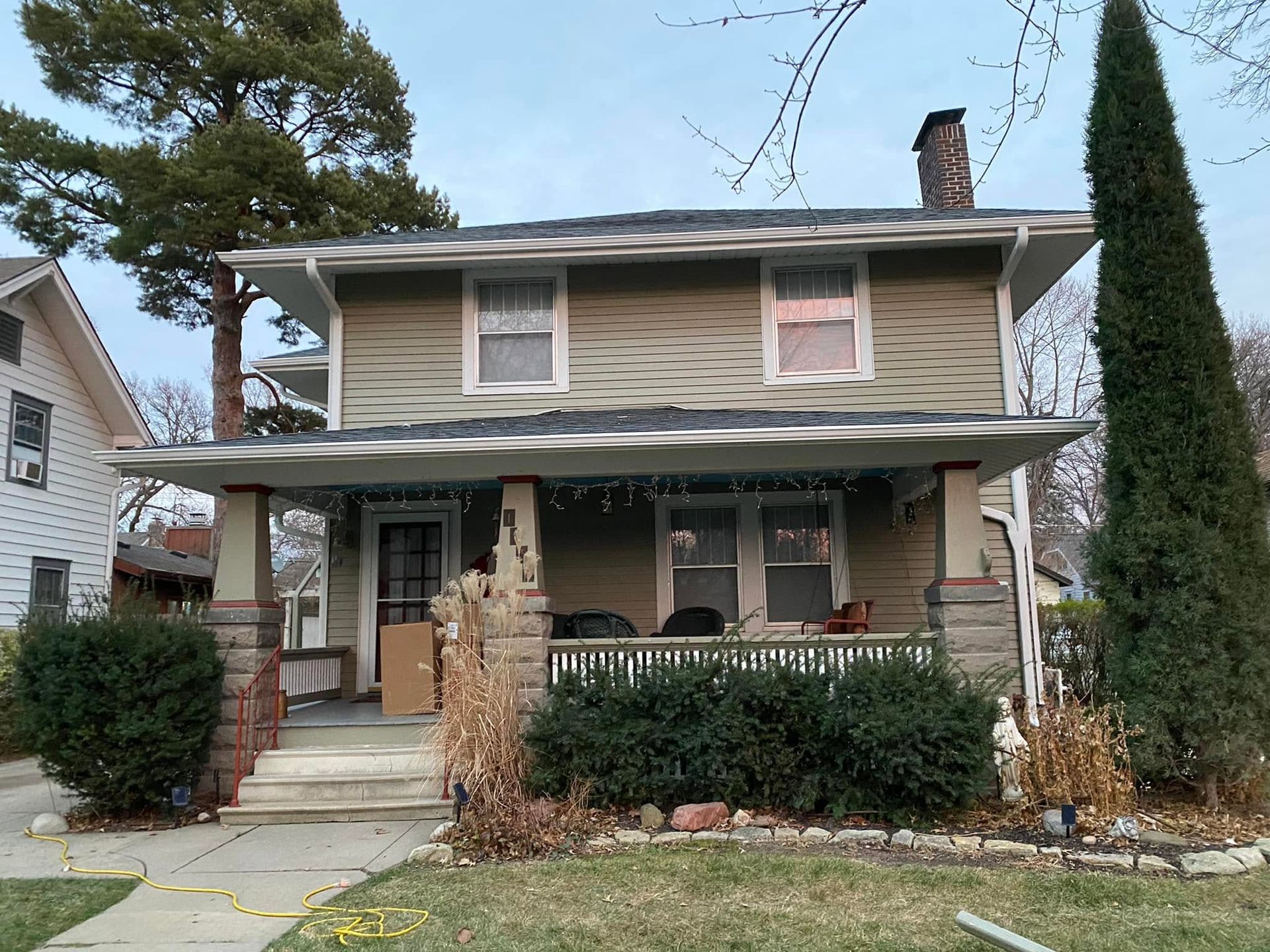 Two-story house with a front porch, stone facade, and trimmed shrubs under an overcast sky