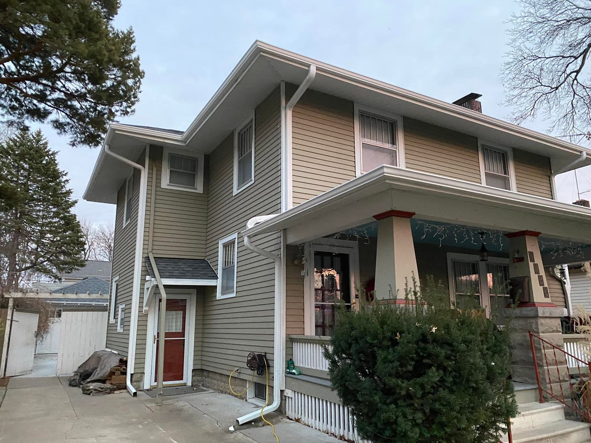 Two-story tan house with white trim and a covered front porch, seen from the side.