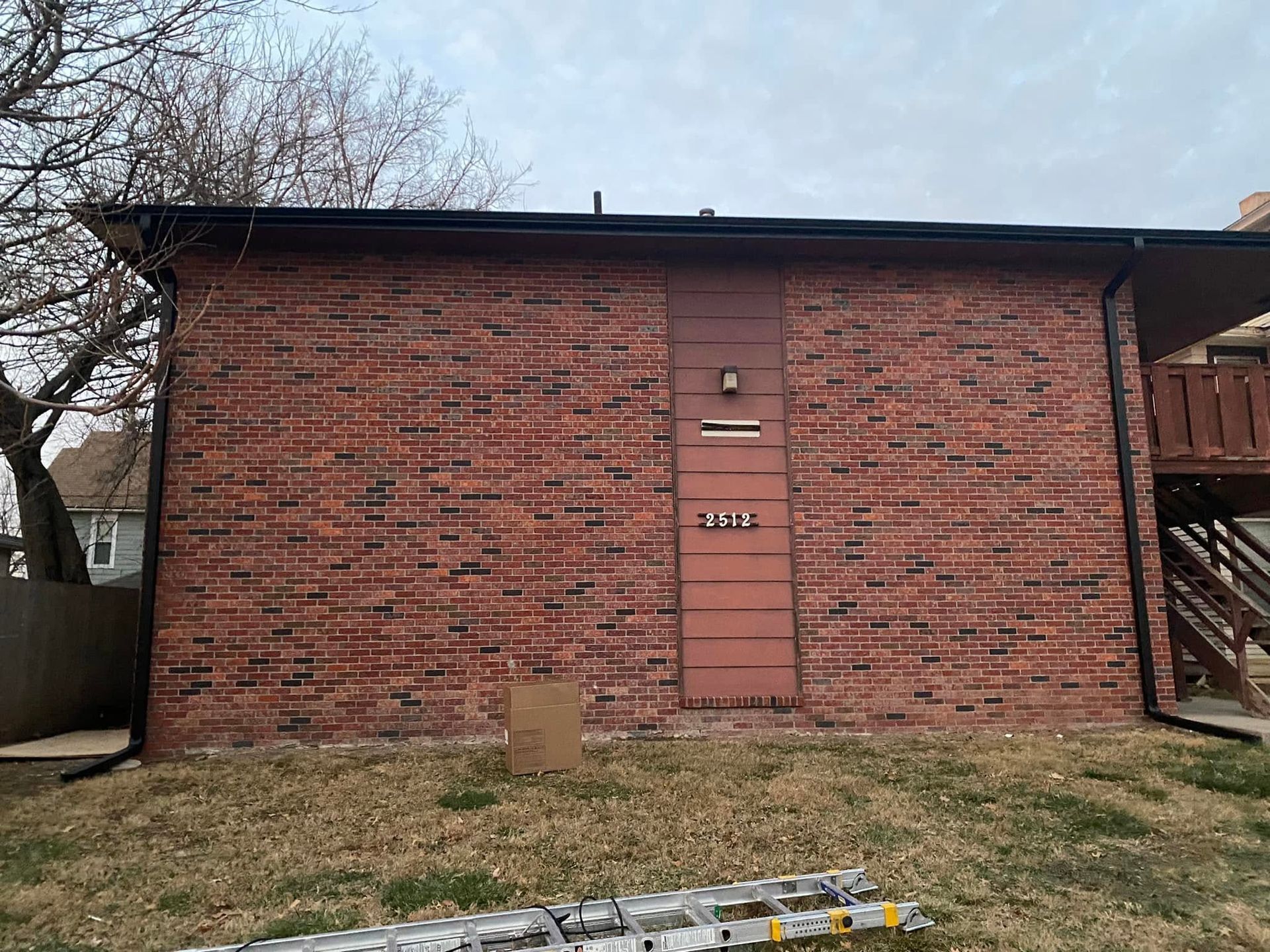 Brick apartment building exterior with a red door, grass yard, and a ladder in front