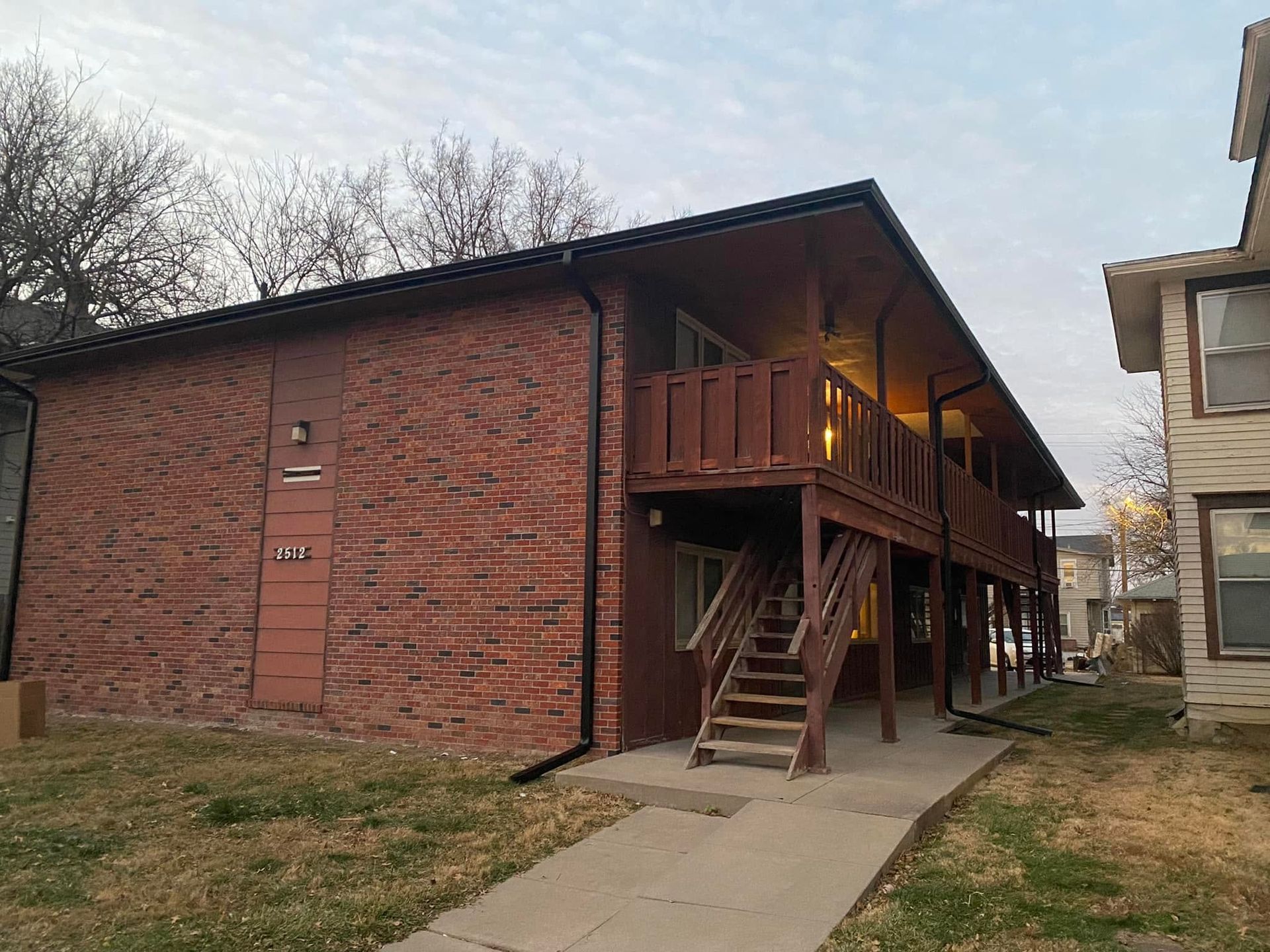 Brick apartment building with exterior wooden stairs and second-floor walkway beside a concrete path