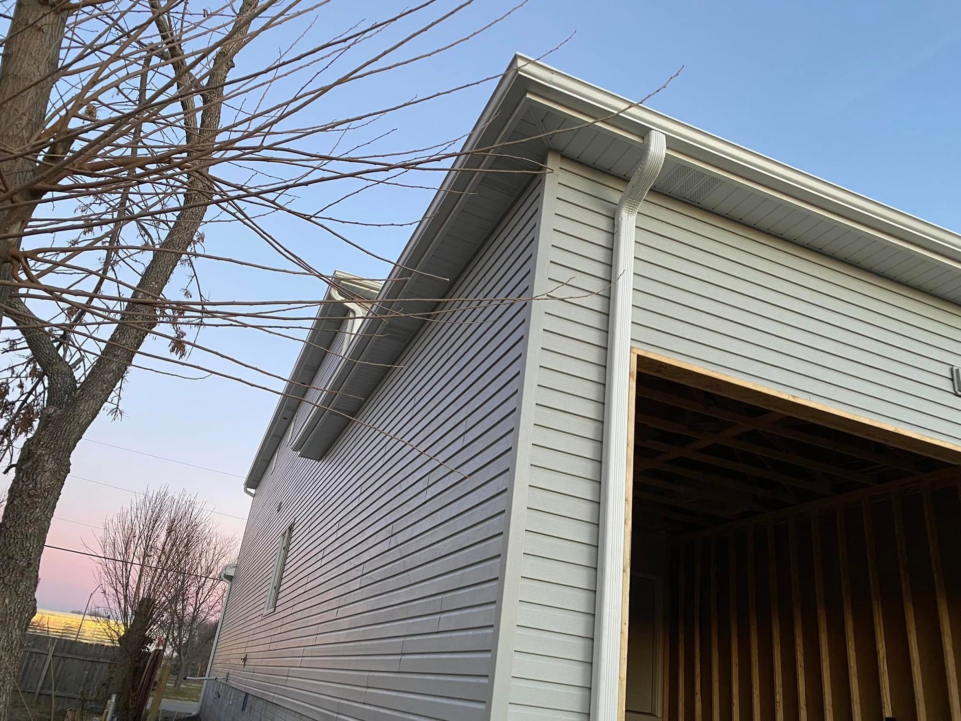 Detached garage with open bay, white siding, and bare tree branches against a dusk sky