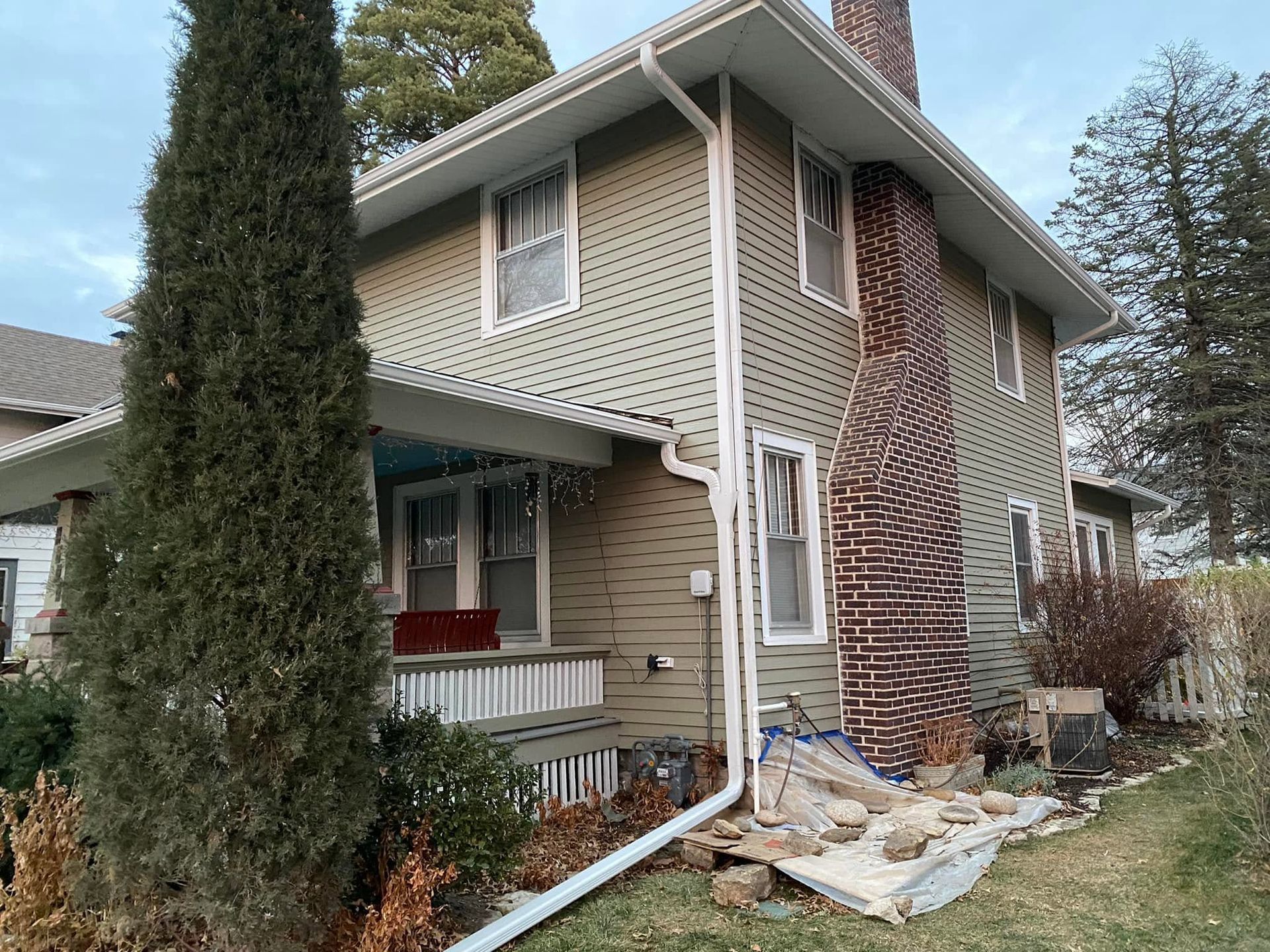 Two-story house with damaged brick siding and debris piled along the front walkway