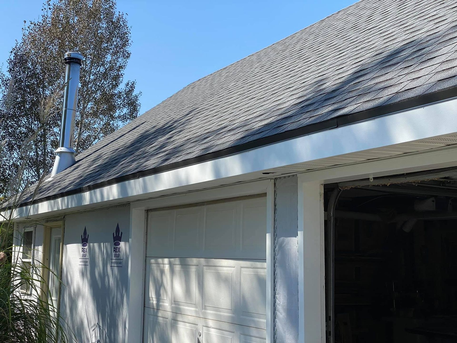 White garage exterior with open door, sloped shingle roof, and a chimney against a tree-lined sky.
