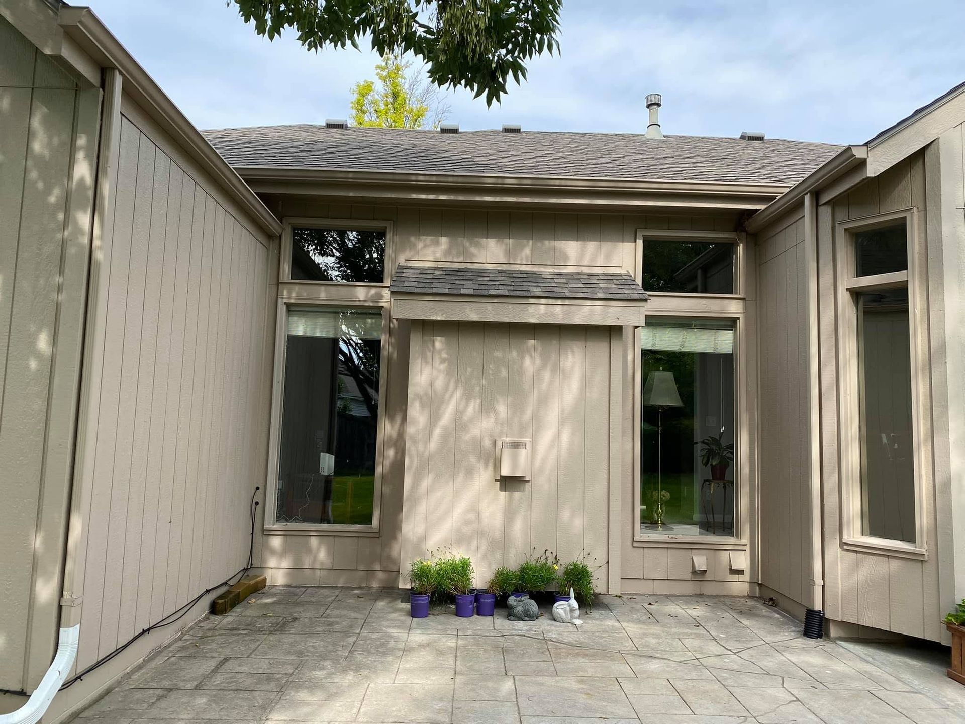 Small courtyard patio with beige stucco walls, windows, potted flowers, and a gray stone floor