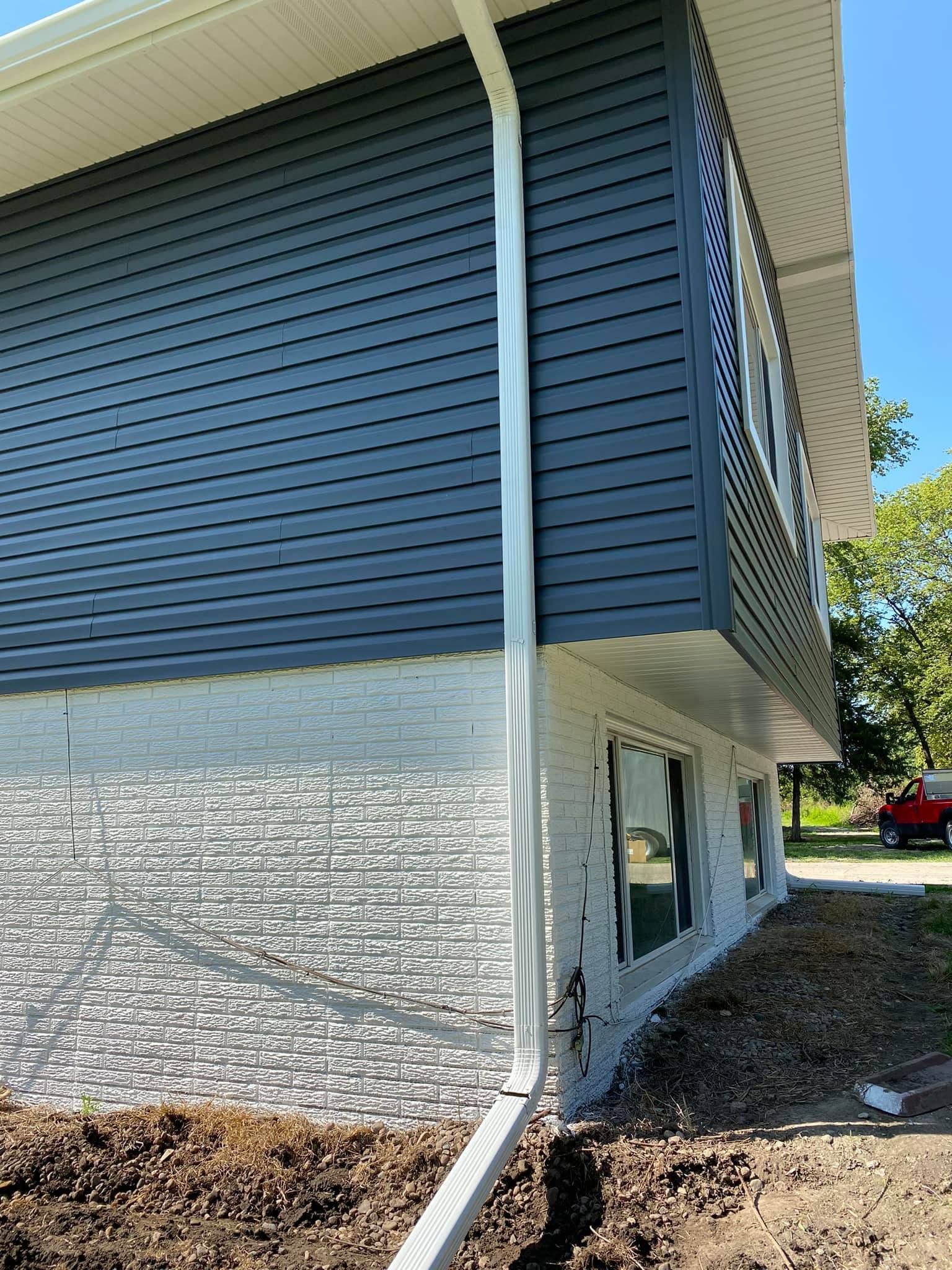 Modern house exterior with white gutter and blue slatted siding above a stone foundation.