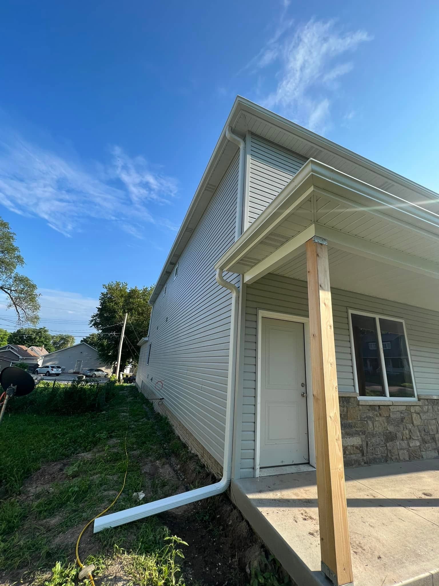 Small house porch with white decorative siding, stone facade, and blue sky overhead