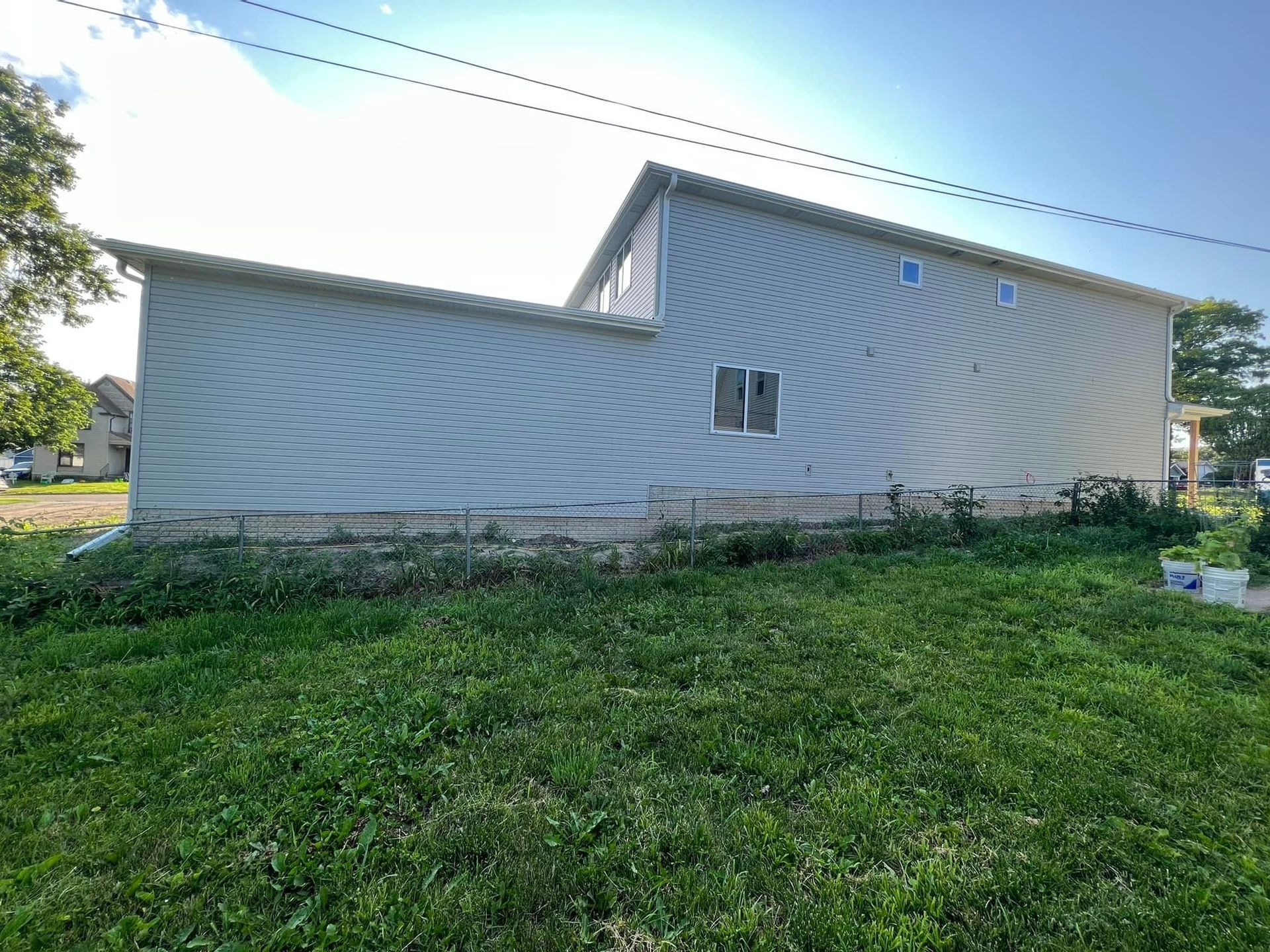 Side view of a beige house with a sloped roof and grassy yard under a clear blue sky
