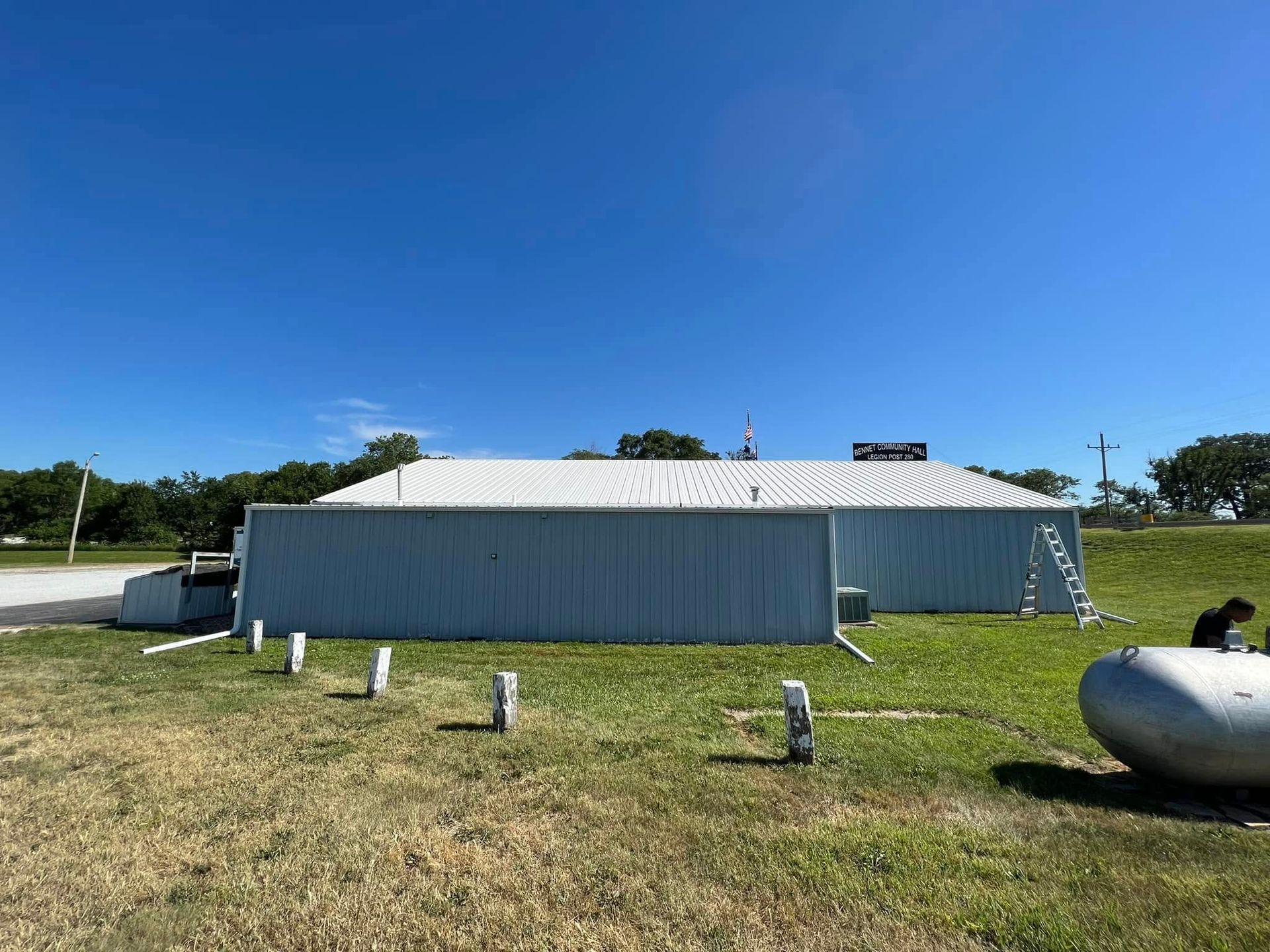 Long silver metal building on a grassy field under a clear blue sky