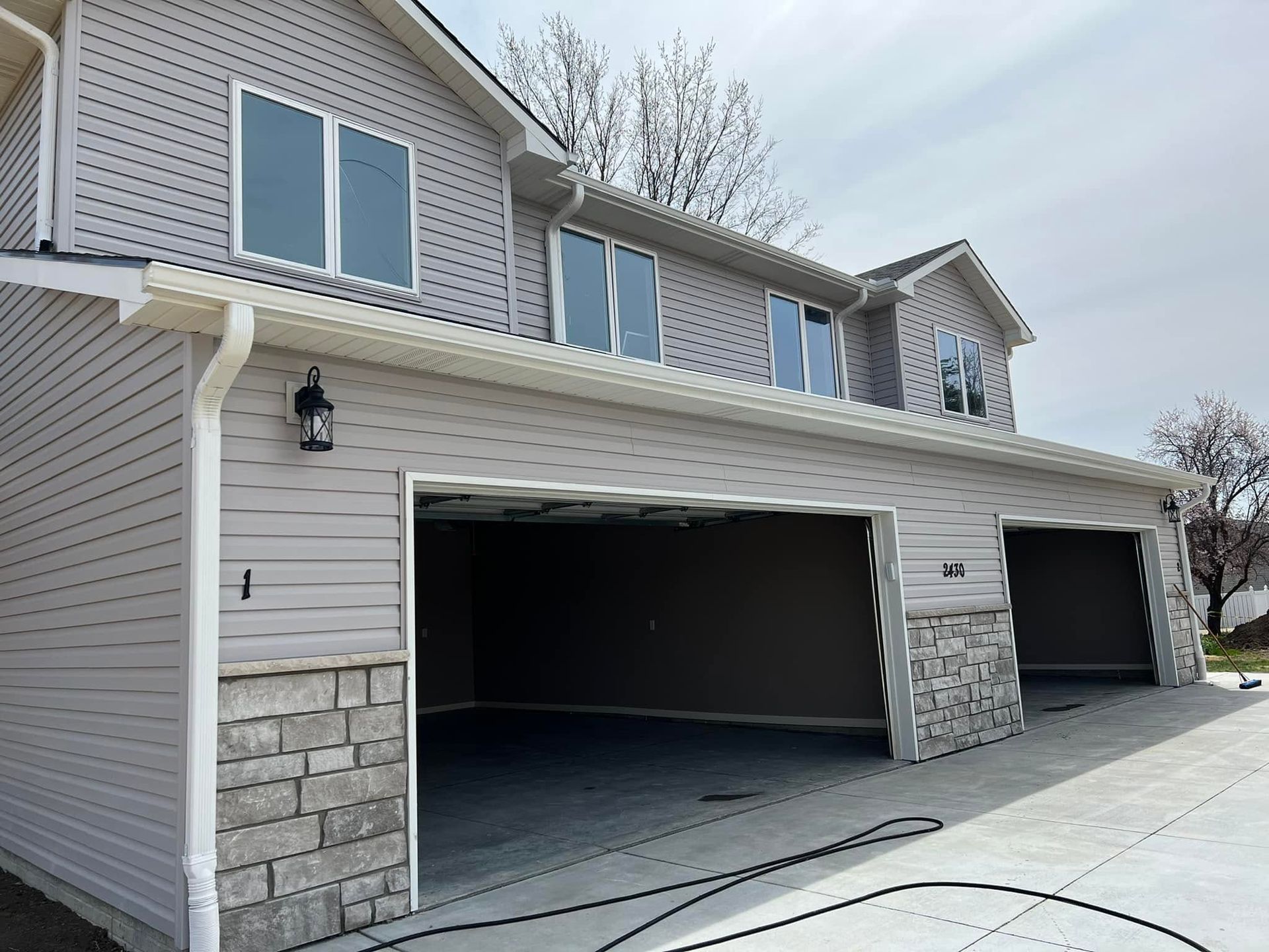 Suburban house exterior with three garage doors, light siding, and stone accents