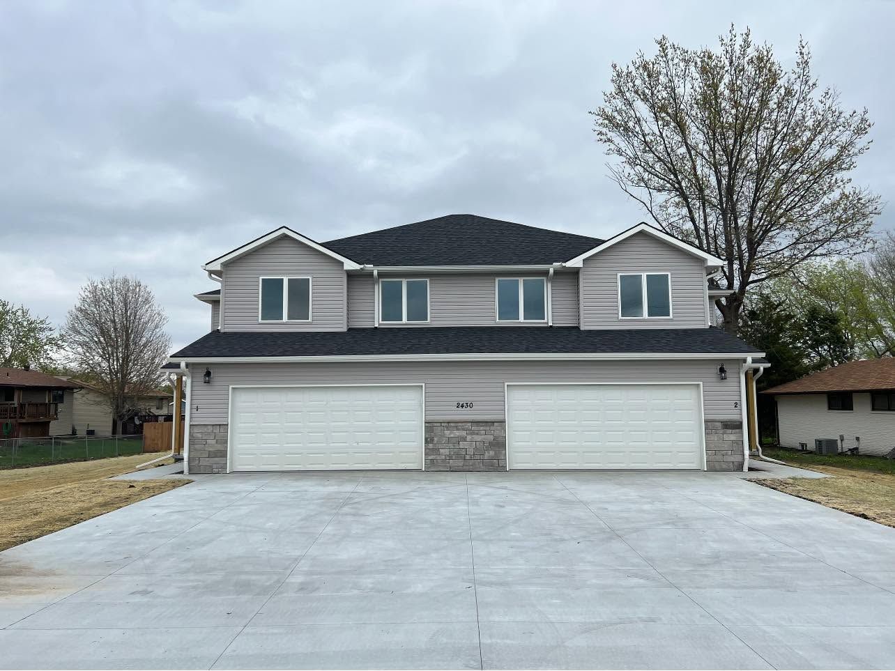 Suburban two-story house with a three-car garage and a wide concrete driveway under a cloudy sky