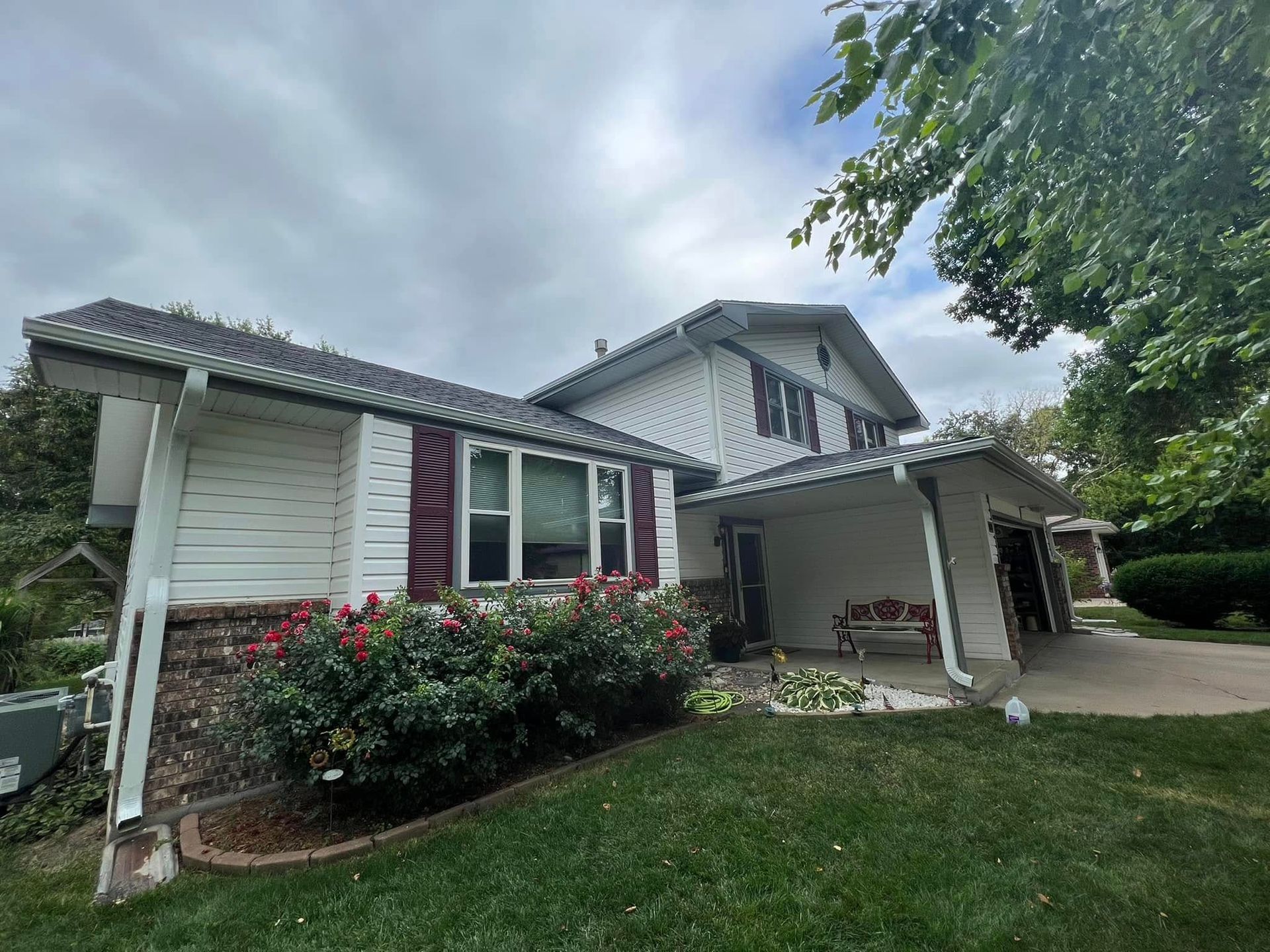 Suburban house exterior with white siding, red shutters, a covered porch, and a driveway under cloudy skies