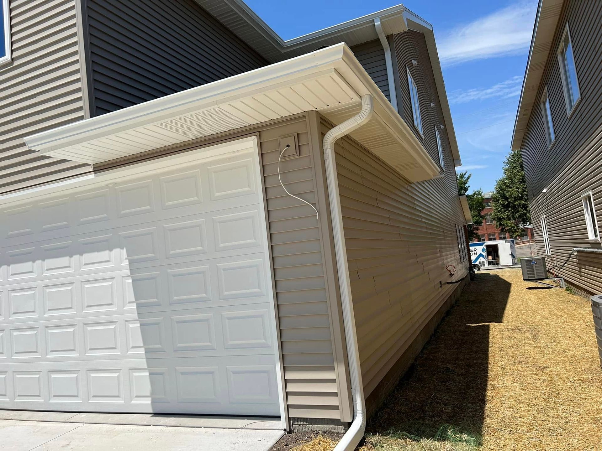 Side view of a beige garage and house with a white garage door and narrow side yard between homes