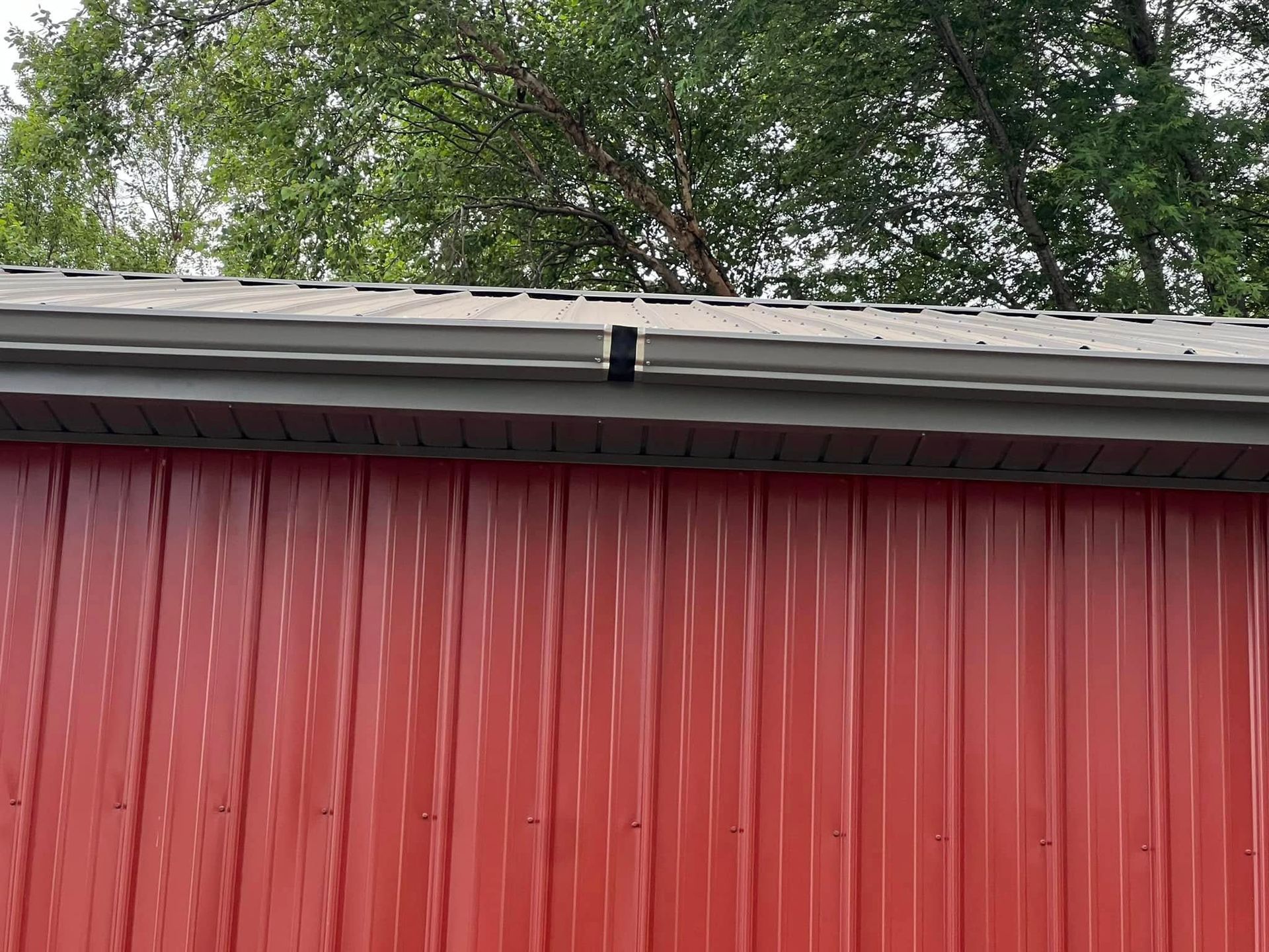 Red corrugated metal wall with gray roof edge and trees above