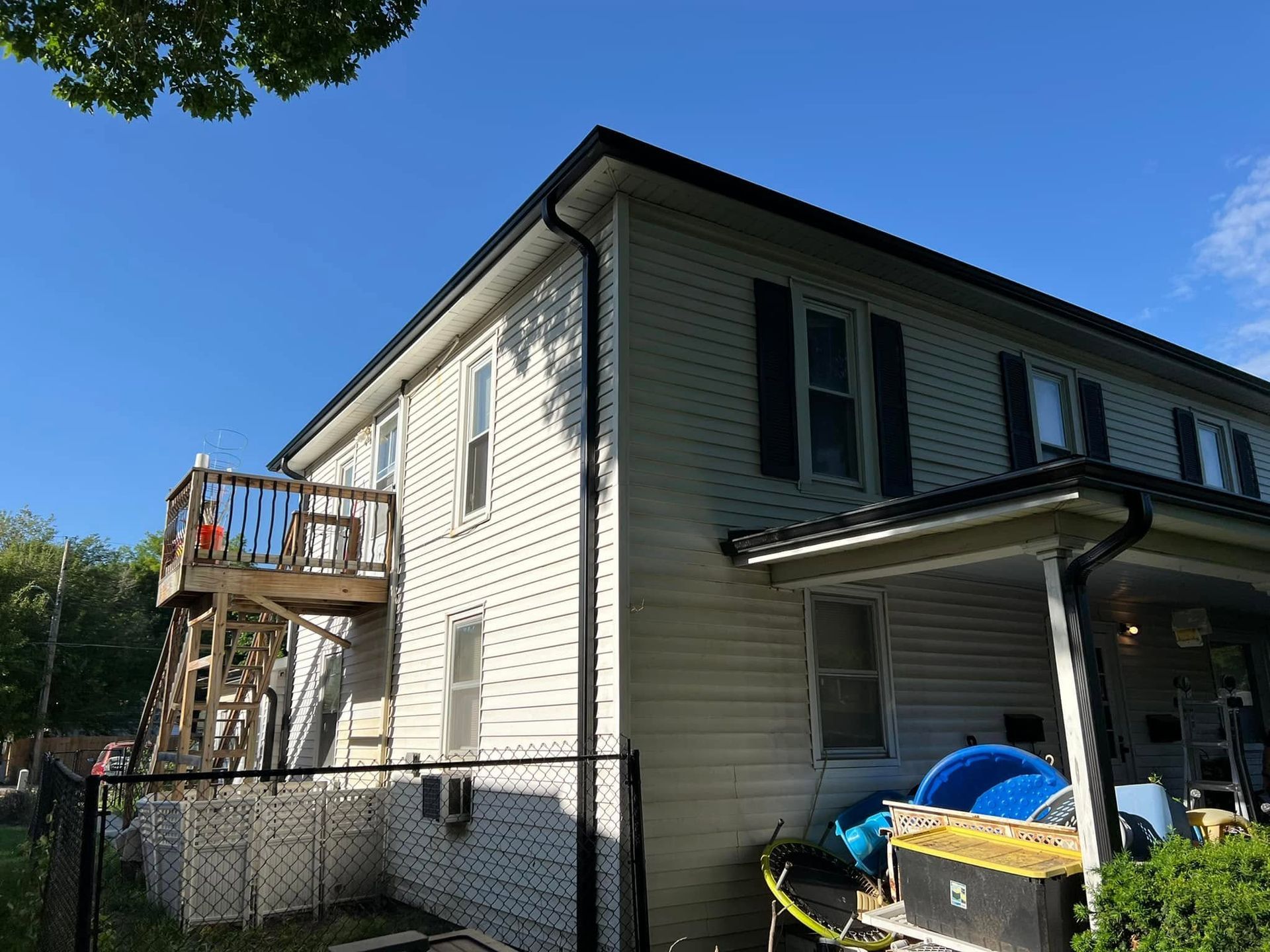 Two-story white house with black shutters, fenced yard, and a wooden deck on the side