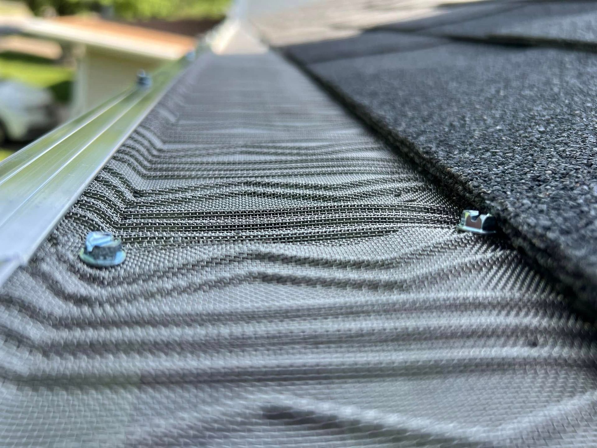 Close-up of a roof gutter guard with water droplets and a shingle edge above it