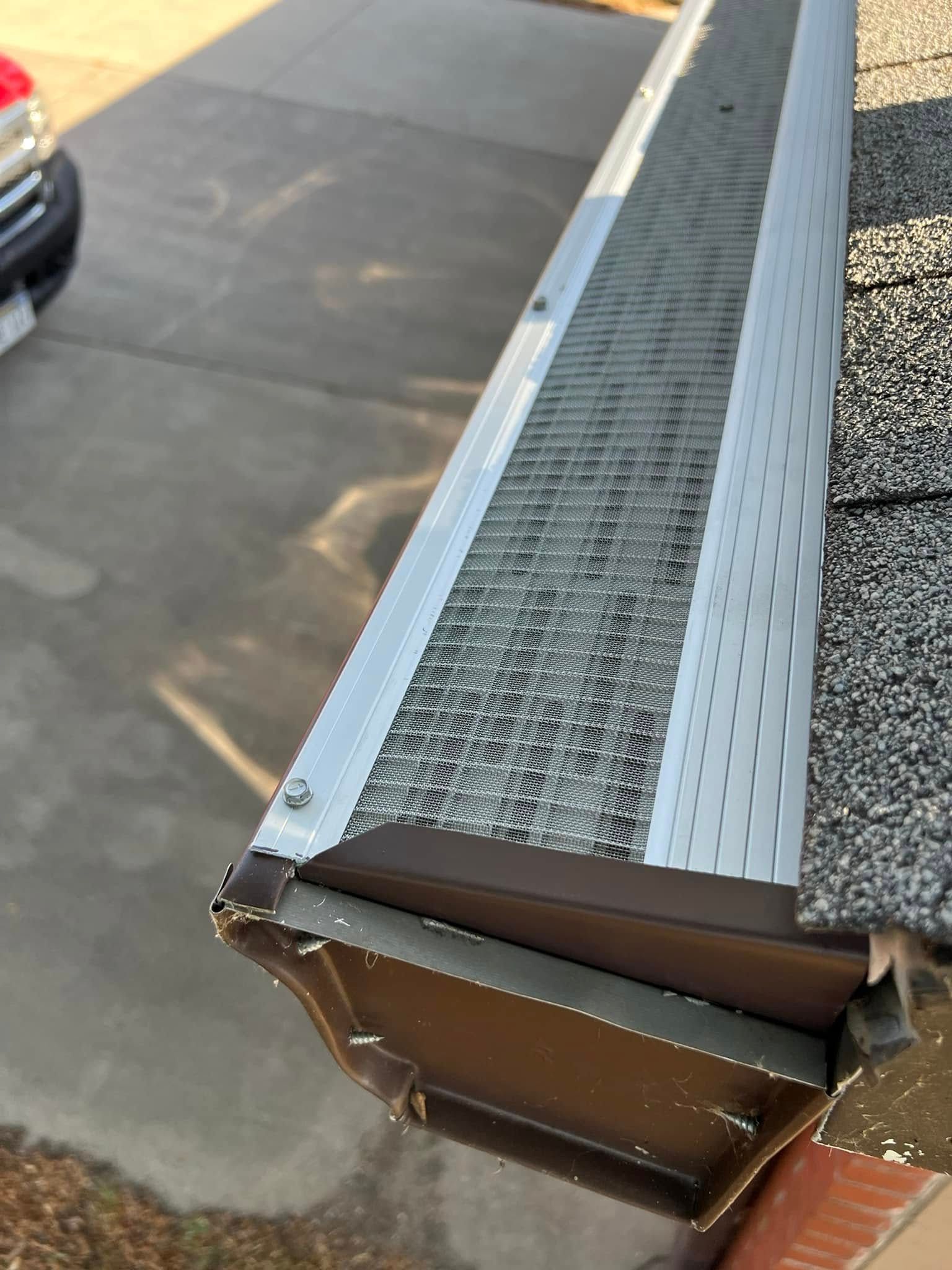 Damaged metal gutter and fascia on a roof edge above a paved driveway