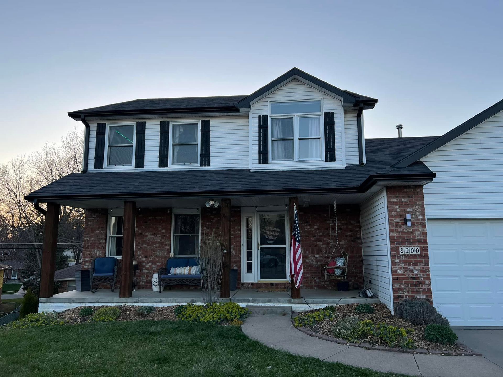 Two-story brick house with white siding, front porch, and an American flag at dusk
