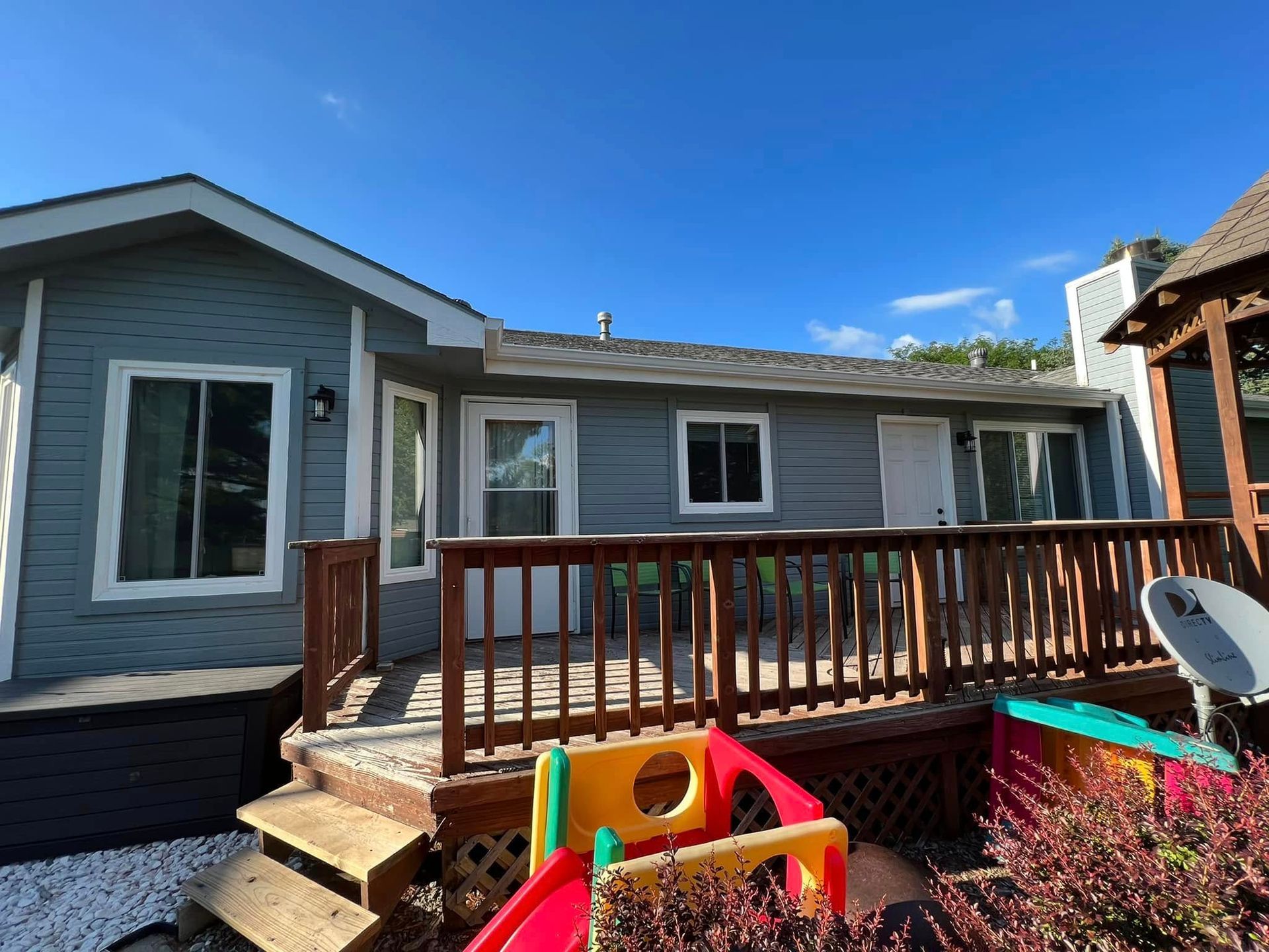 Backyard deck on a gray house with wooden railing and colorful children's toys in front